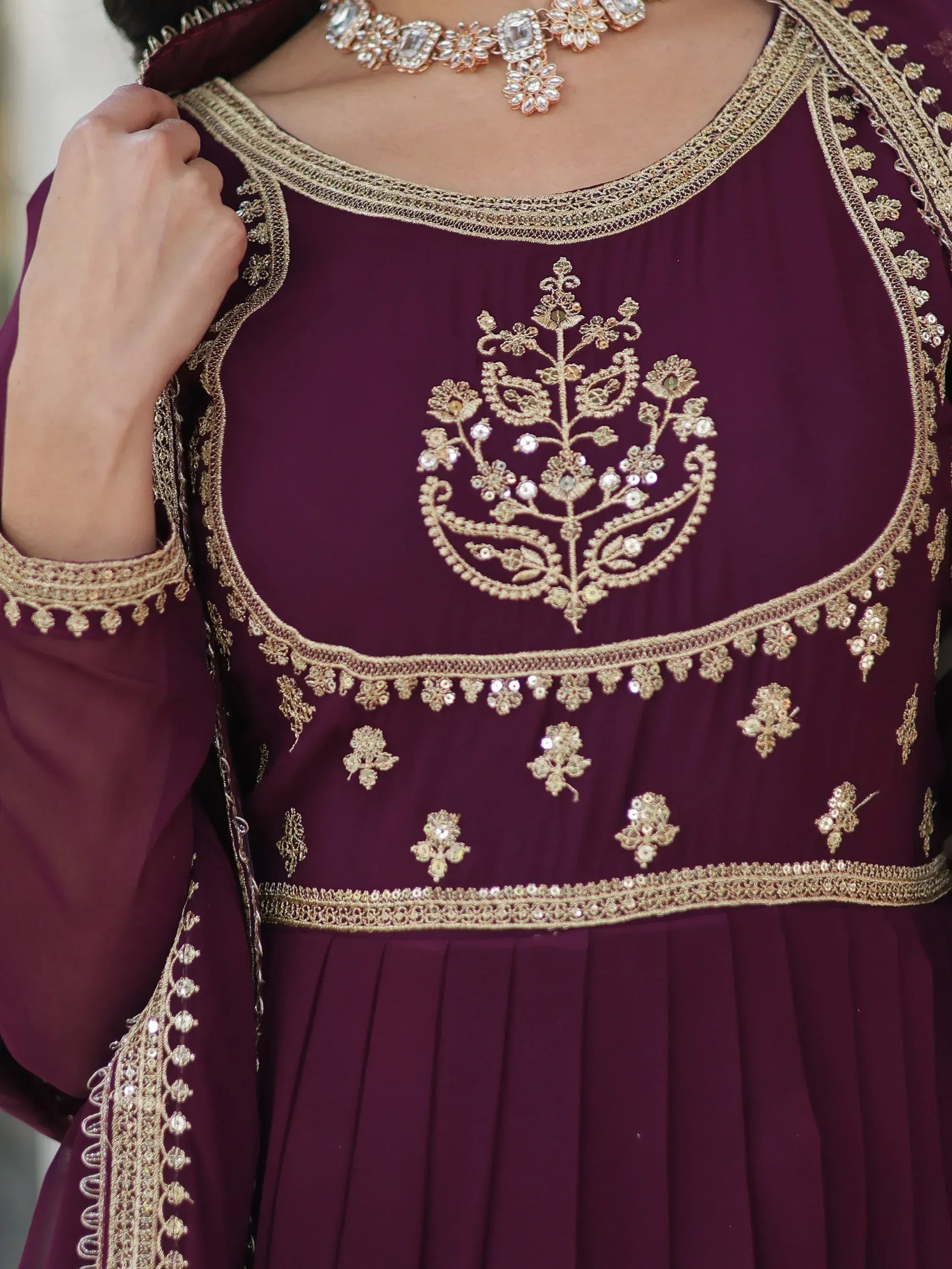 Elegant maroon ethnic gown with gold floral embroidery and sequin detailing, paired with statement jewelry.