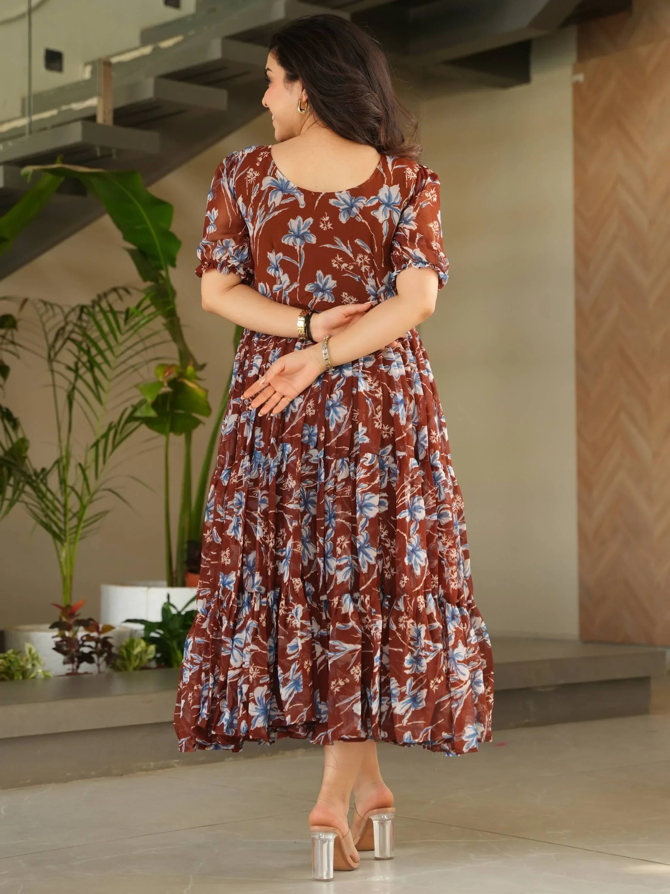 Woman in brown floral maxi dress with puff sleeves and transparent heels indoors