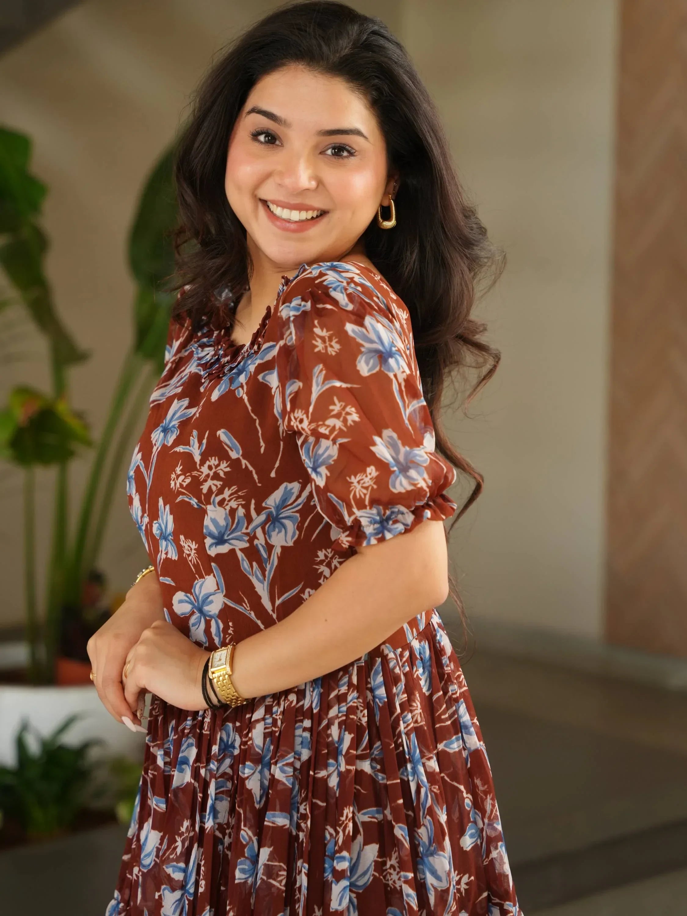 Smiling woman in a brown floral ethnic dress with blue and white patterns, indoor setting