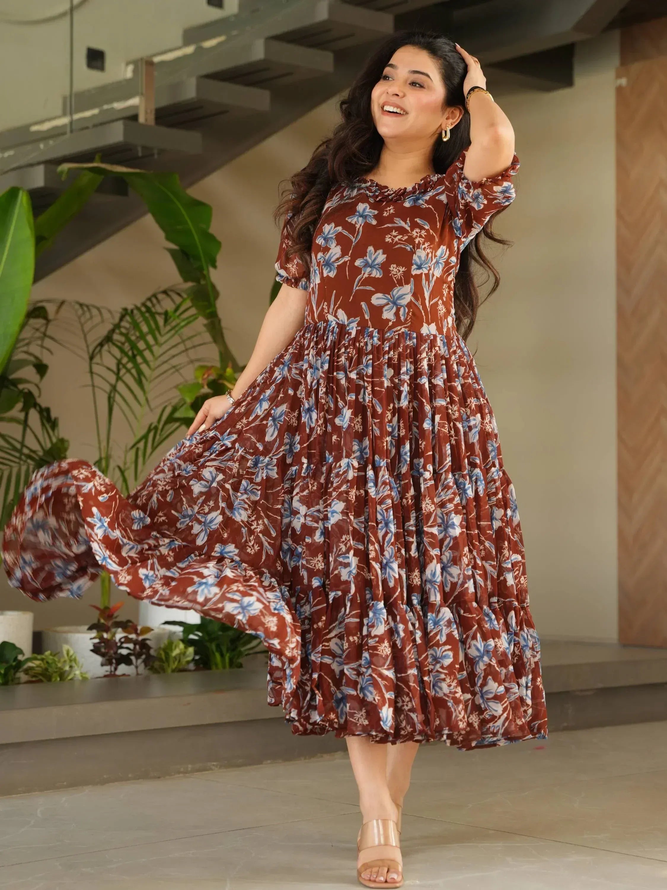 Woman in brown floral ethnic gown with blue print, pleated skirt, and puff sleeves, perfect for Indian occasions.