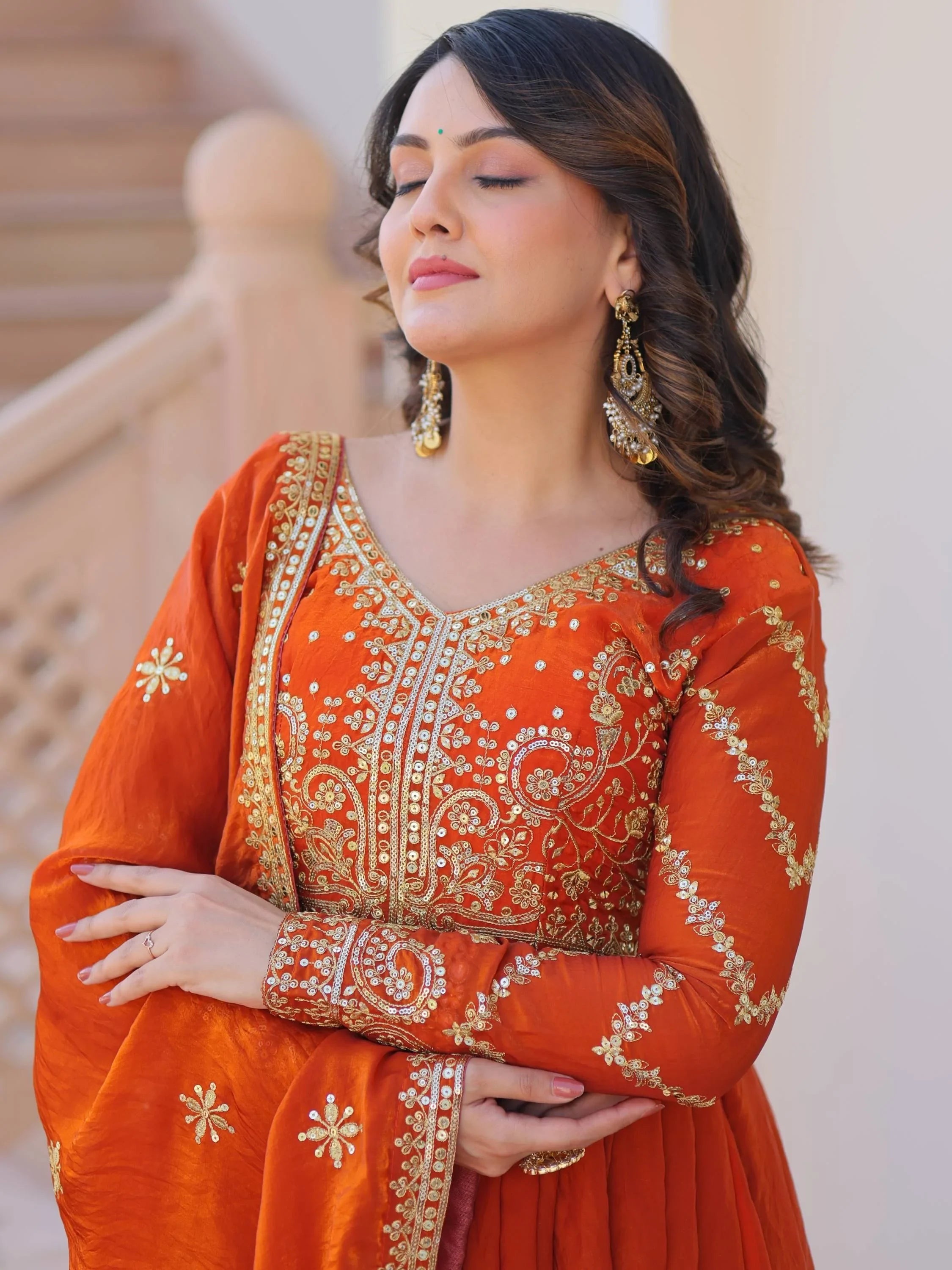 Woman in orange ethnic gown with gold embroidery, wearing statement earrings