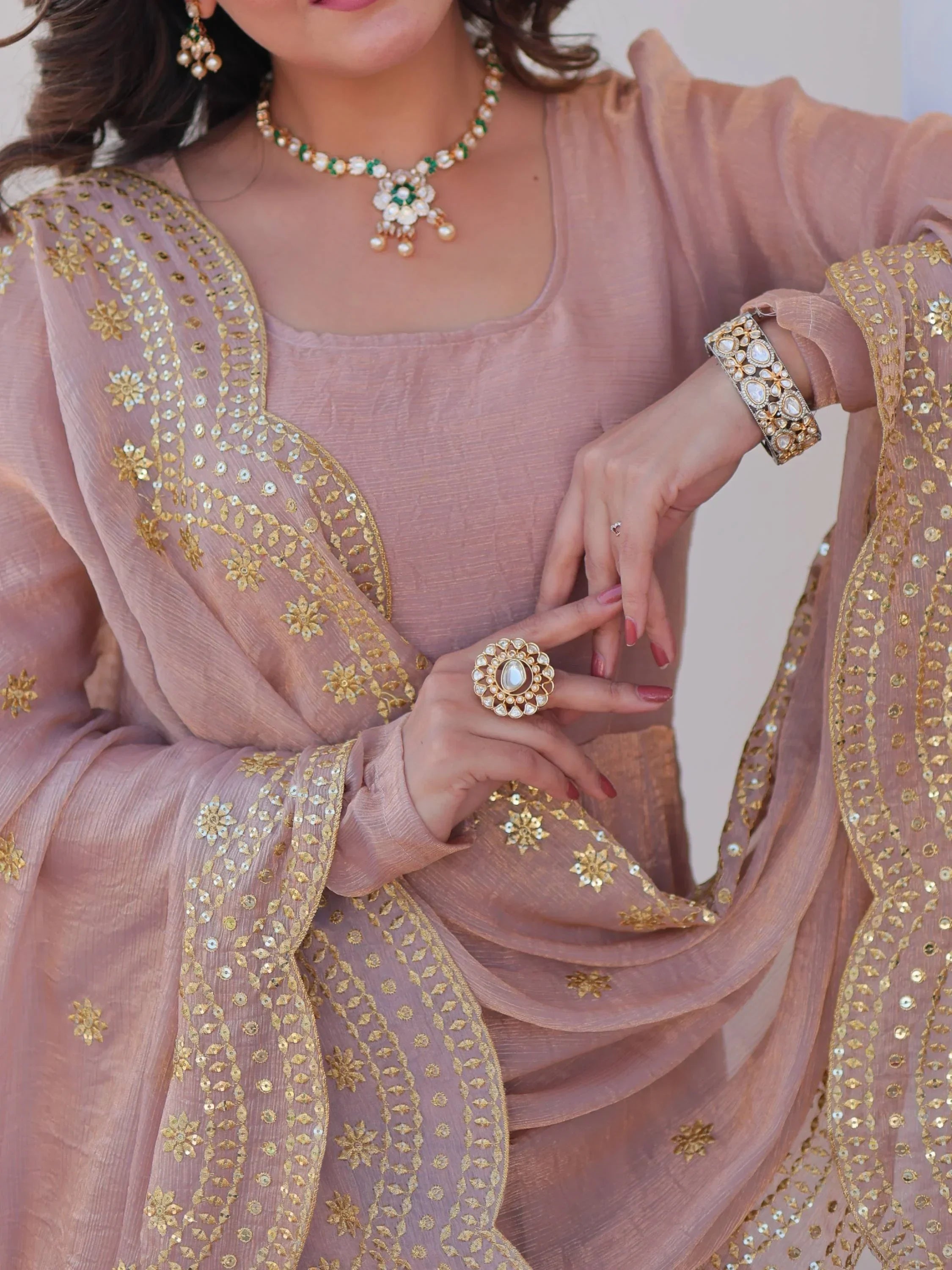 Woman wearing embellished chiku color ethnic suit with gold embroidery and traditional jewelry