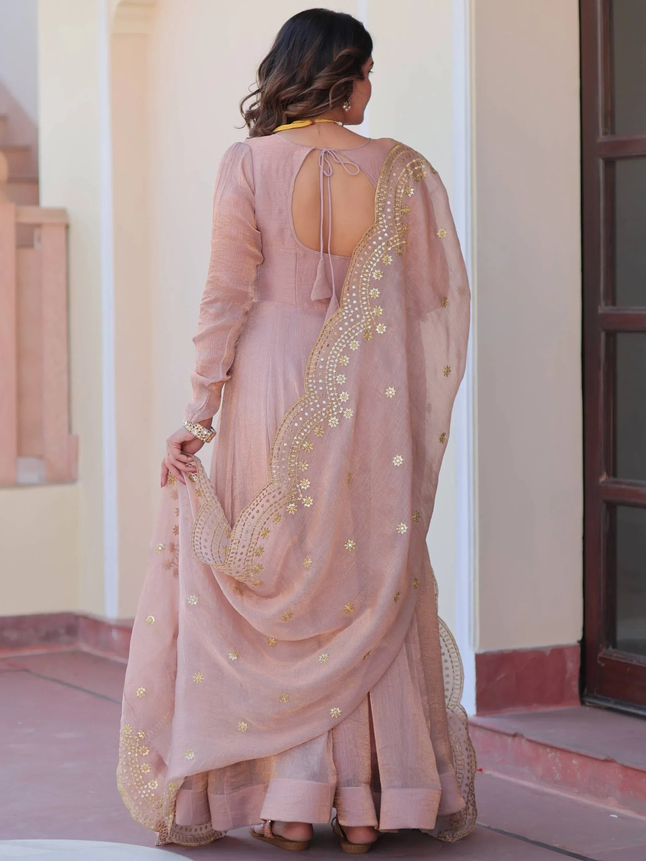 Woman wearing light brown embroidered ethnic lehenga choli with dupatta, back view