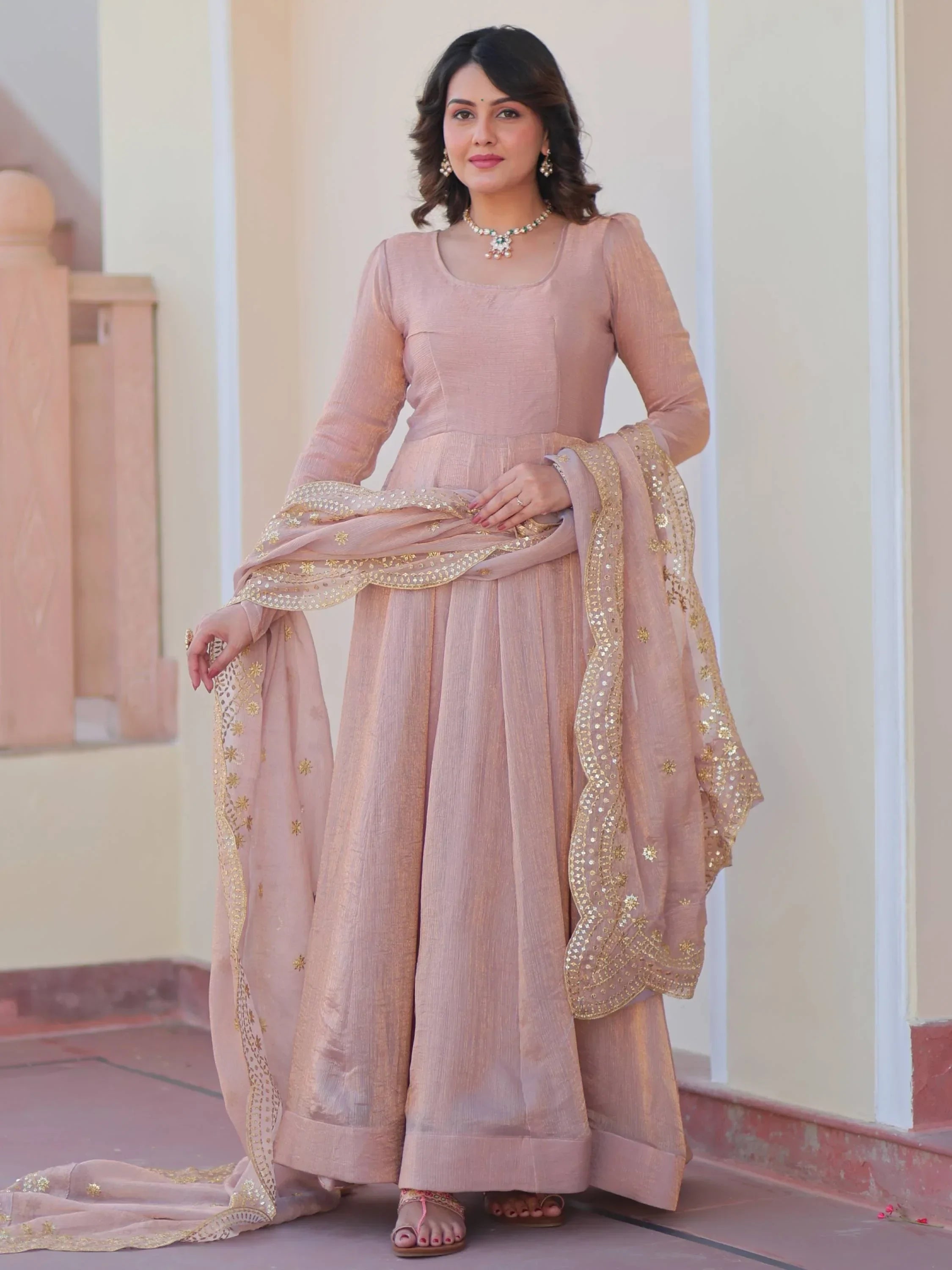 Woman wearing light brown ethnic gown with gold embroidered dupatta, traditional jewelry