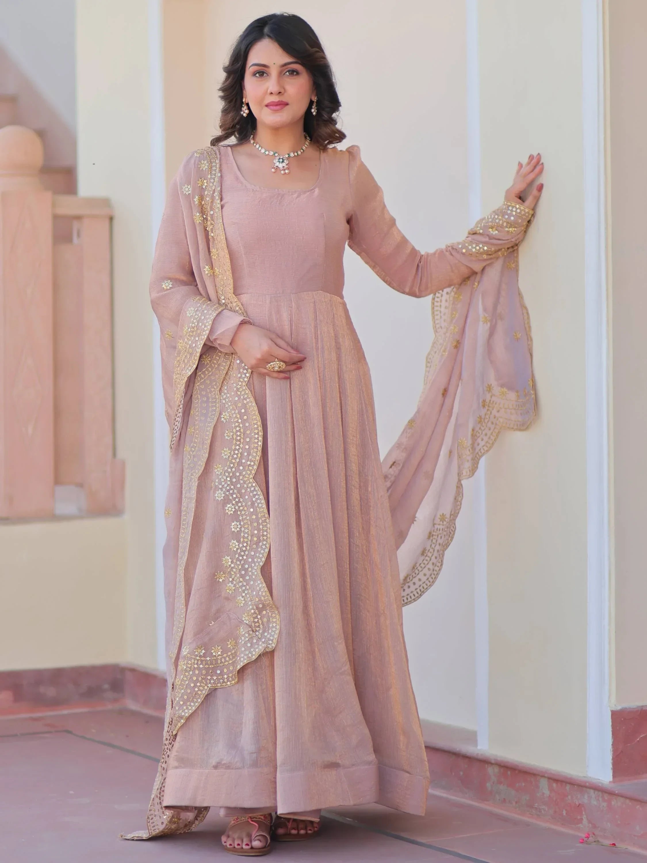 Woman wearing a peach ethnic gown with gold embroidered dupatta, standing outdoors