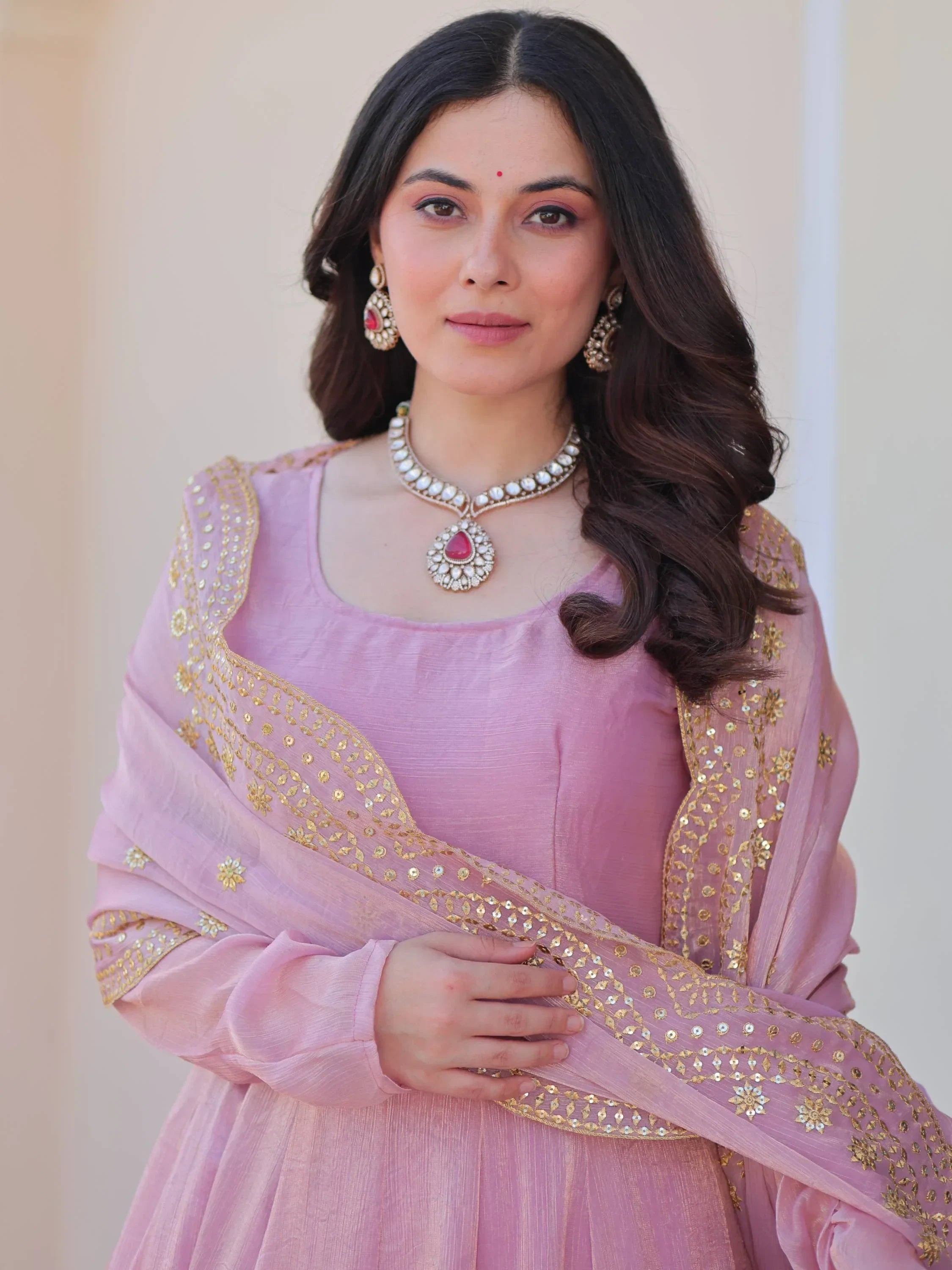 Woman in pink embroidered ethnic gown with gold accents and traditional jewelry