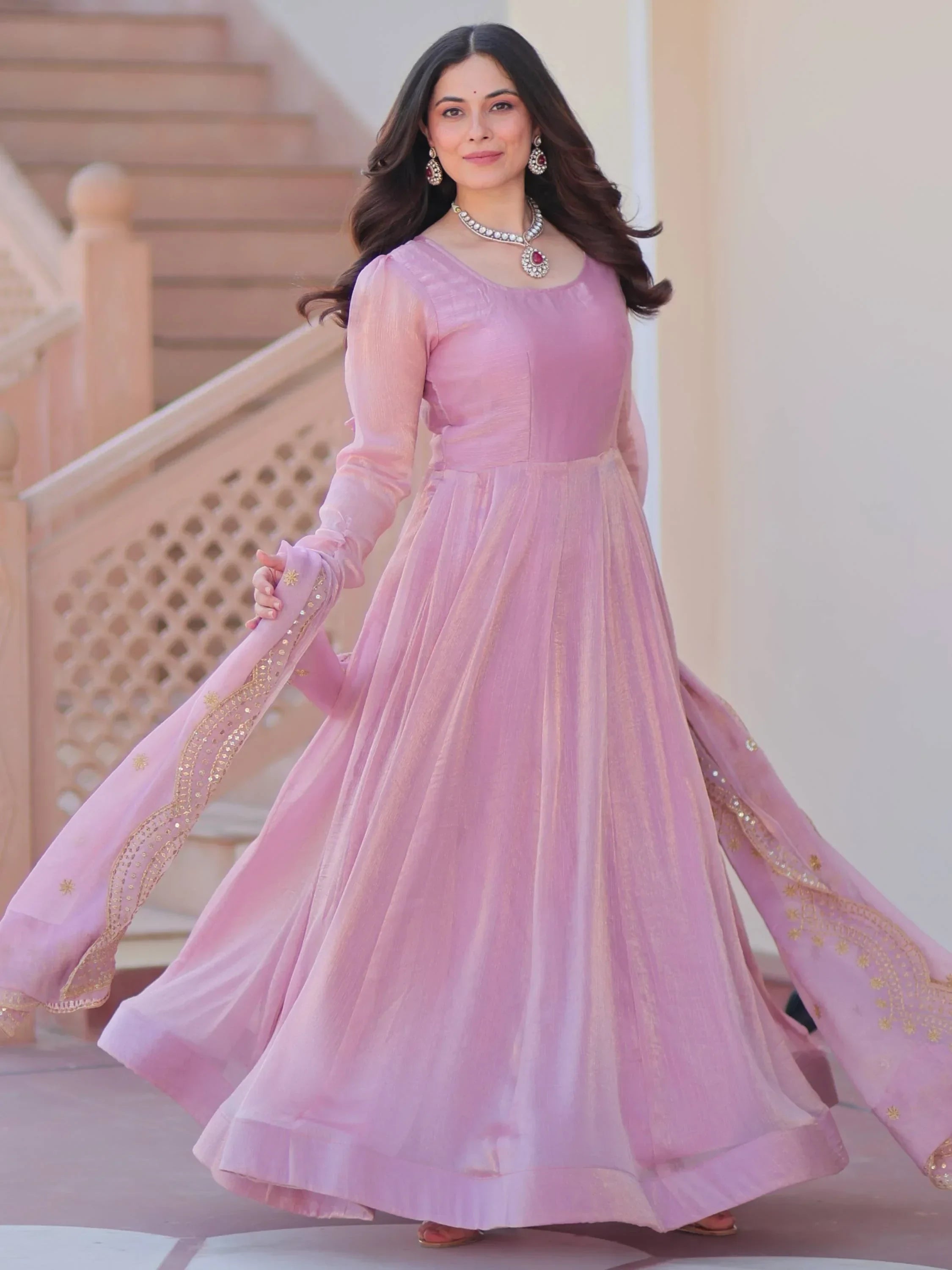 Woman in light pink ethnic gown with gold embroidery, matching dupatta, and jewelry