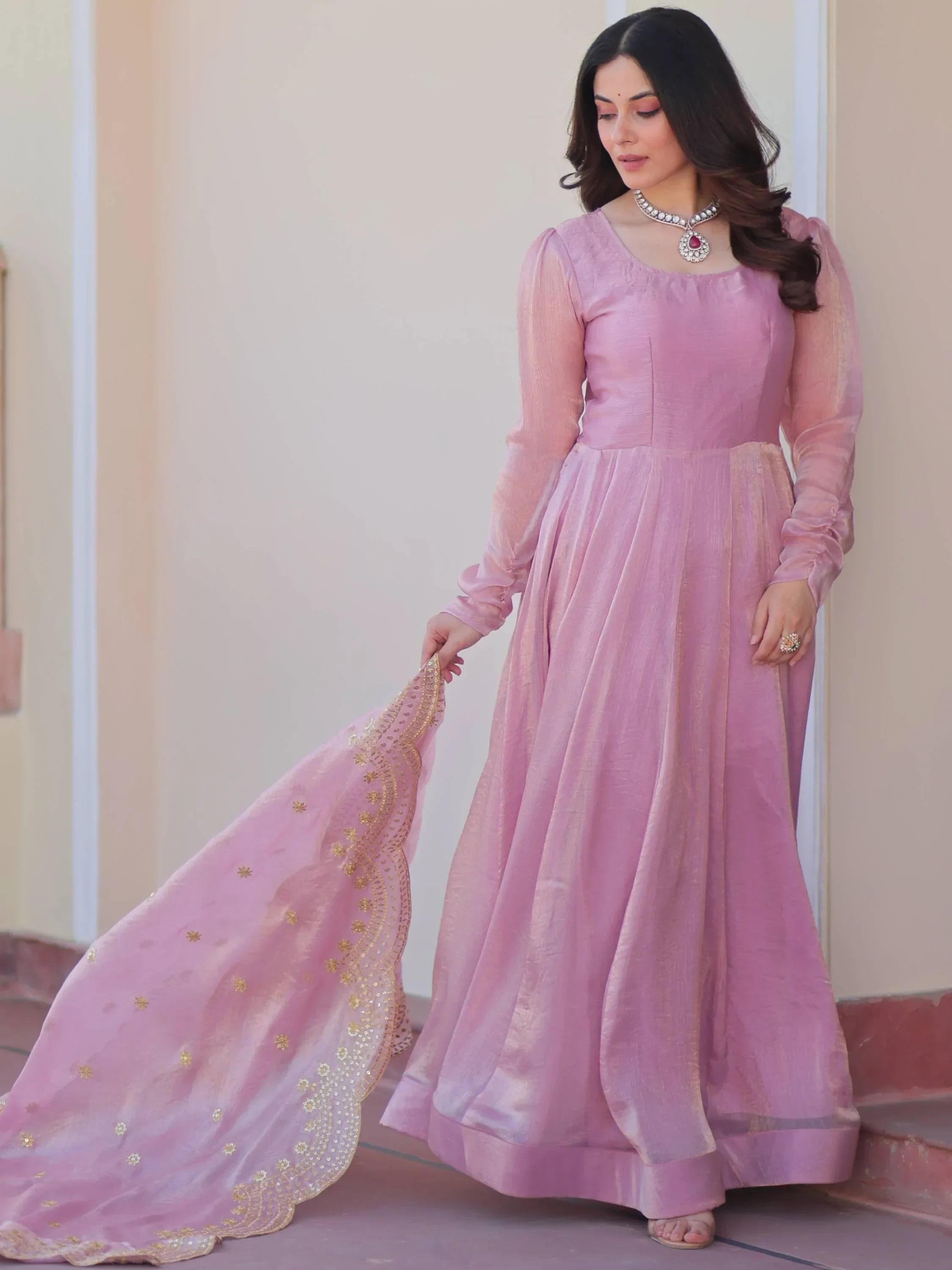 Woman in a pink ethnic gown with gold embroidered dupatta, long sleeves, and statement necklace