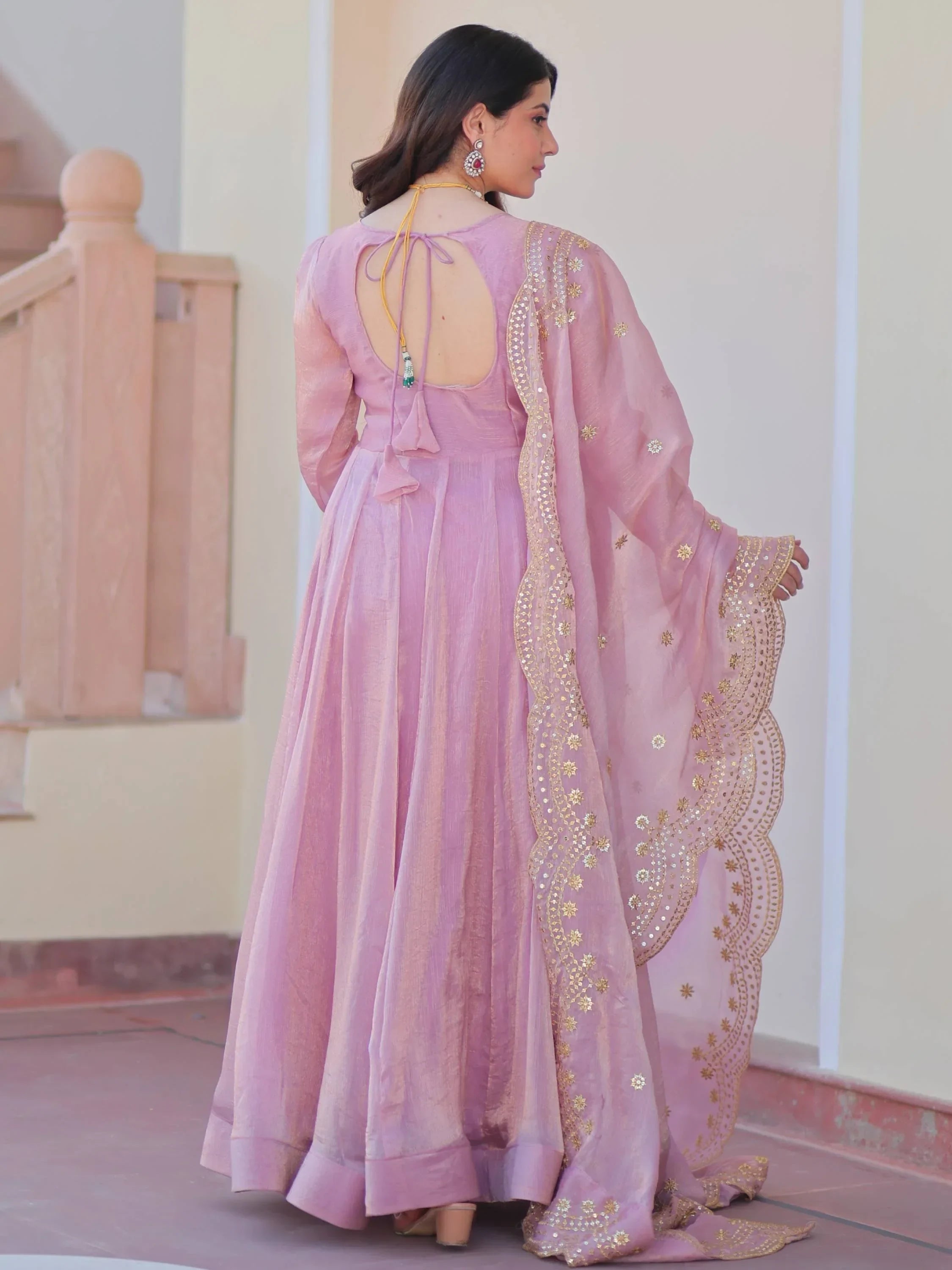 Woman wearing a pink ethnic gown with gold embroidered dupatta, standing outdoors