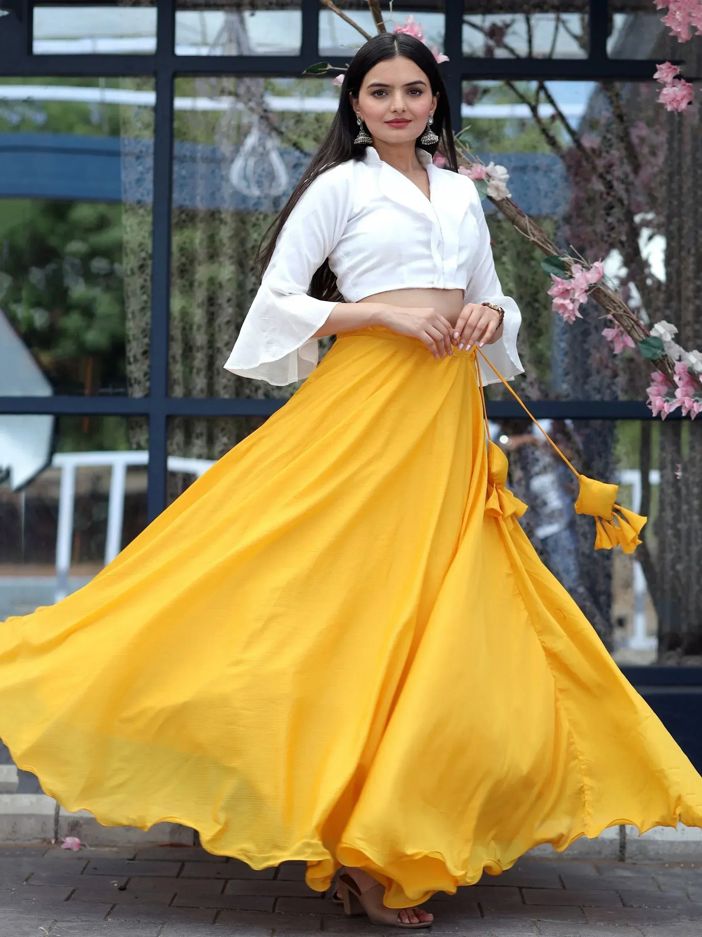 Woman in white crop top and flowing yellow skirt, ethnic wear outfit with floral backdrop