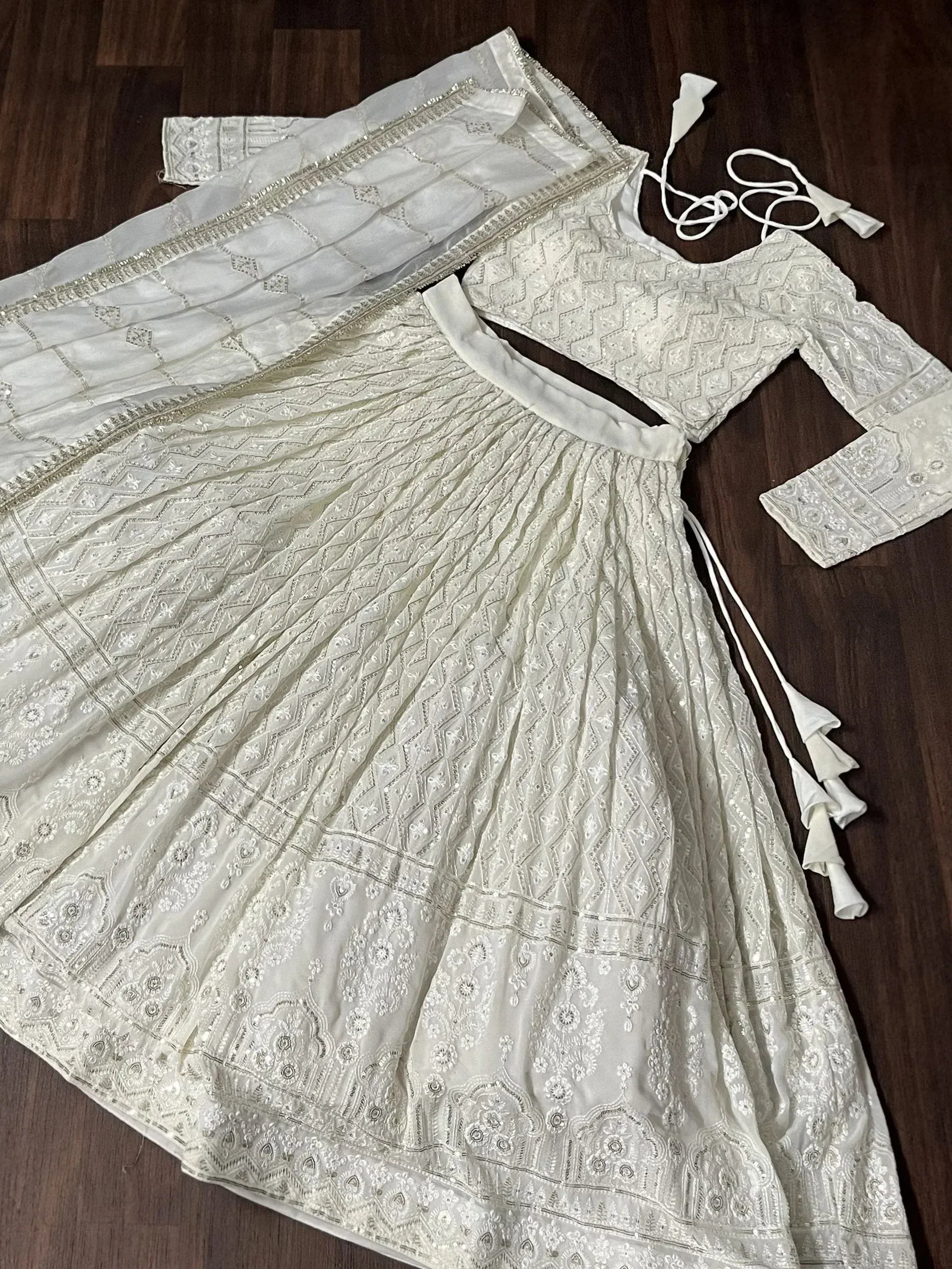 White embroidered lehenga choli with dupatta, featuring intricate geometric patterns and tassel details.