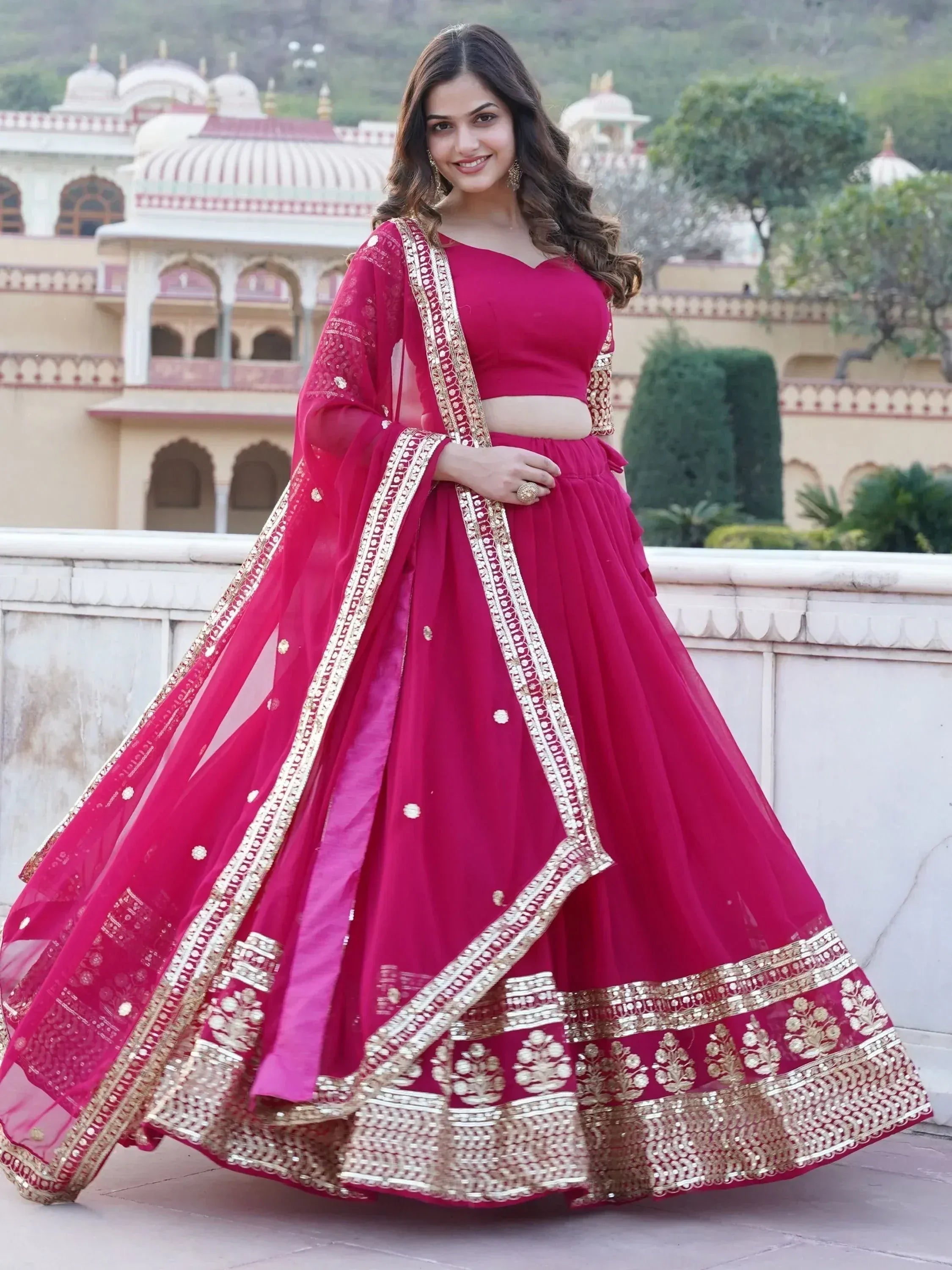 Woman in vibrant pink lehenga choli with gold embroidery, perfect for Indian weddings and festive occasions.