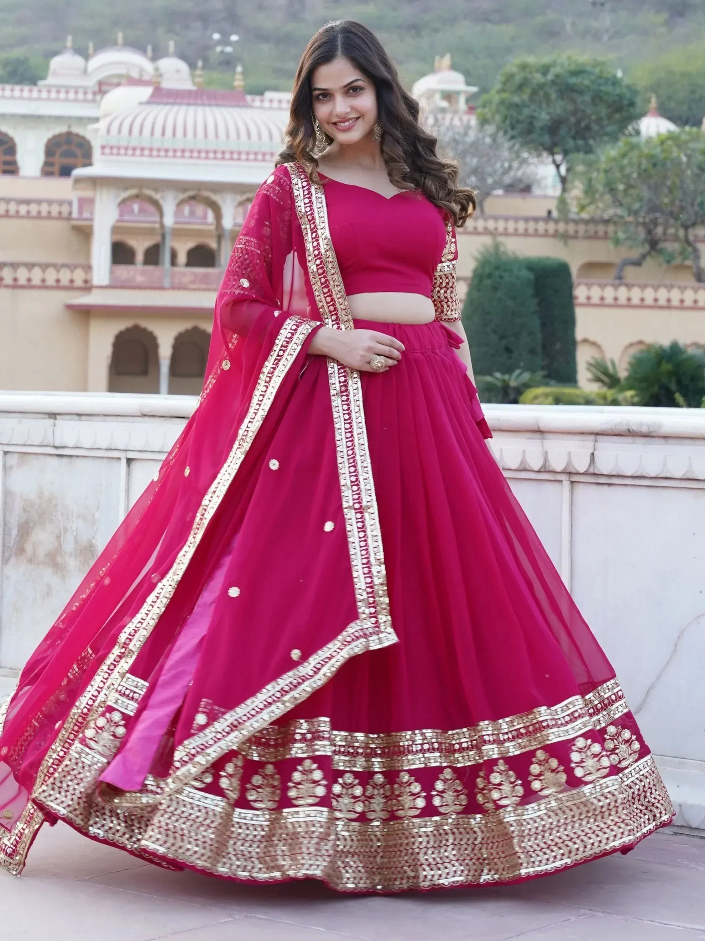 Woman in vibrant pink designer lehenga choli with gold embroidery, perfect for Indian ethnic wear occasions