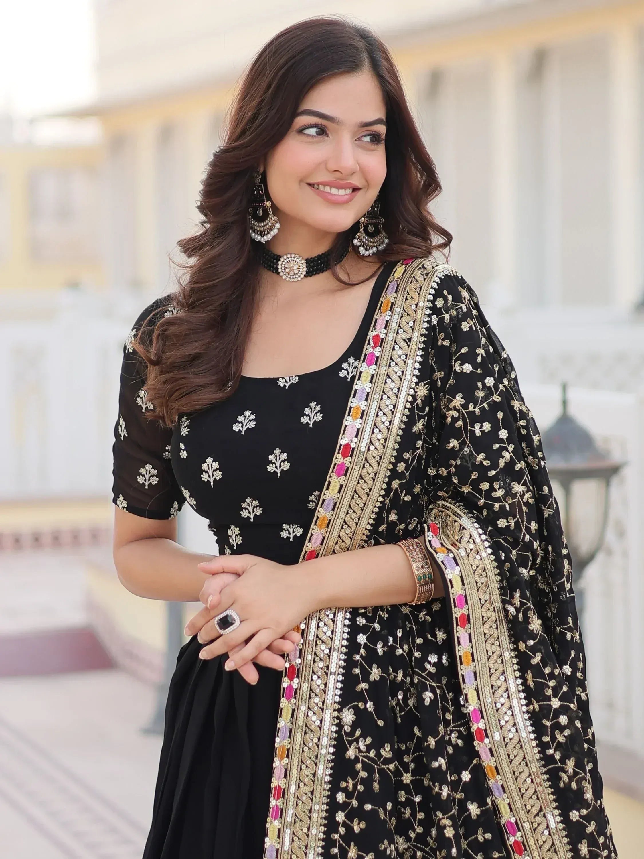 Black embroidered ethnic gown with gold floral detailing and colorful sequin border, paired with statement jewelry