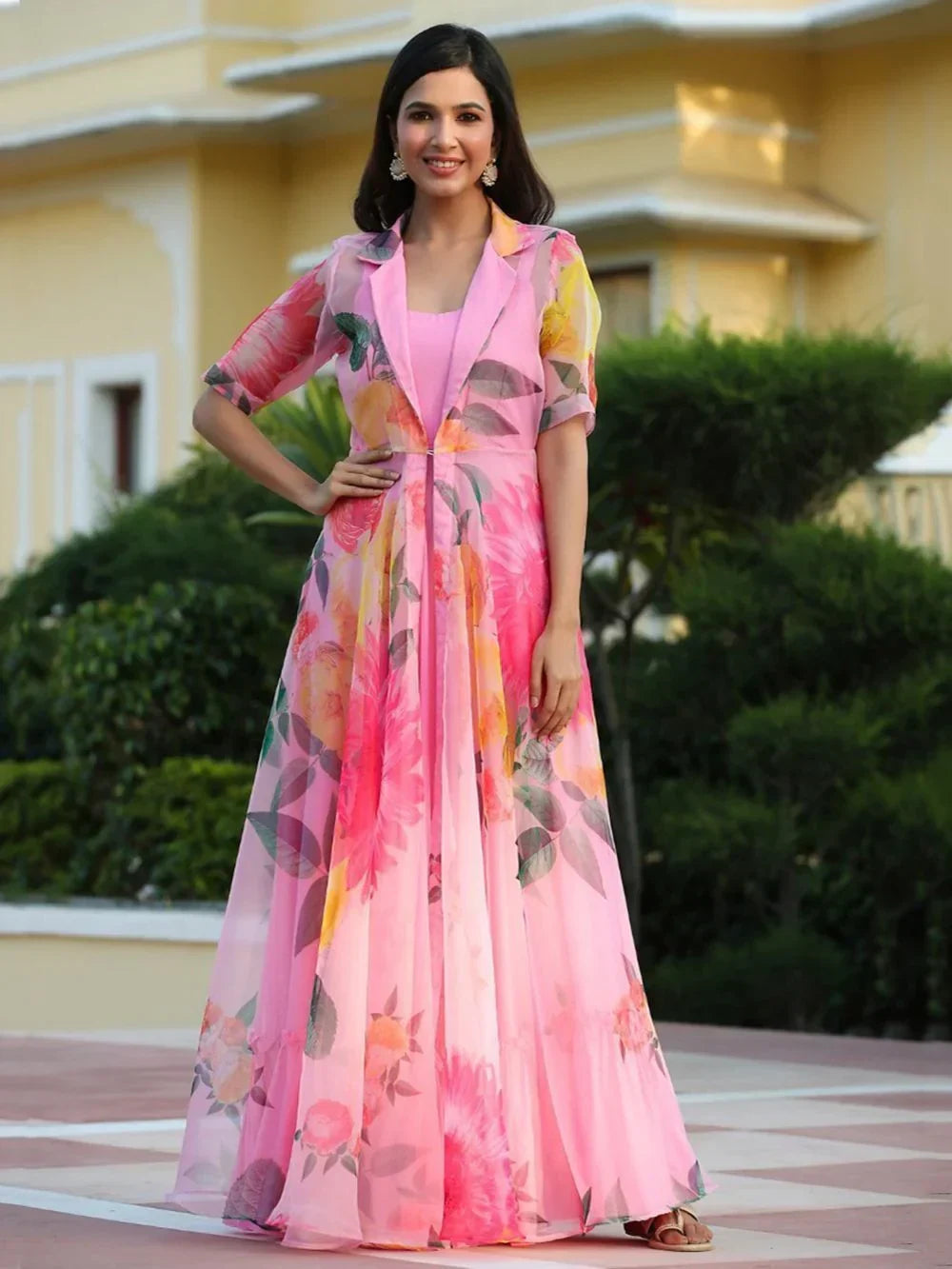 Woman wearing a pink floral long ethnic gown, standing outdoors in sunlight