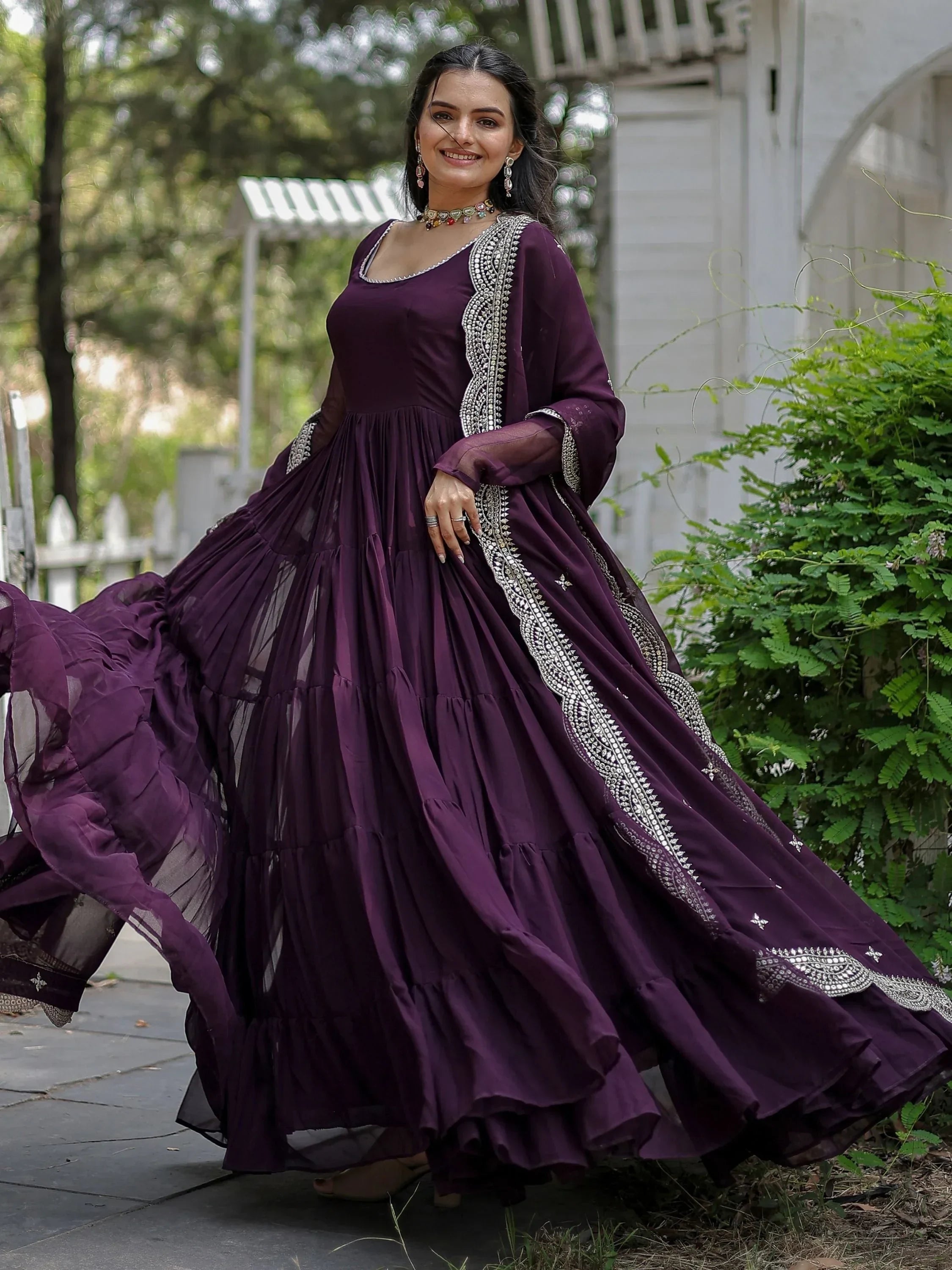 Woman in a flowy purple ethnic gown with silver embroidery, posing outdoors