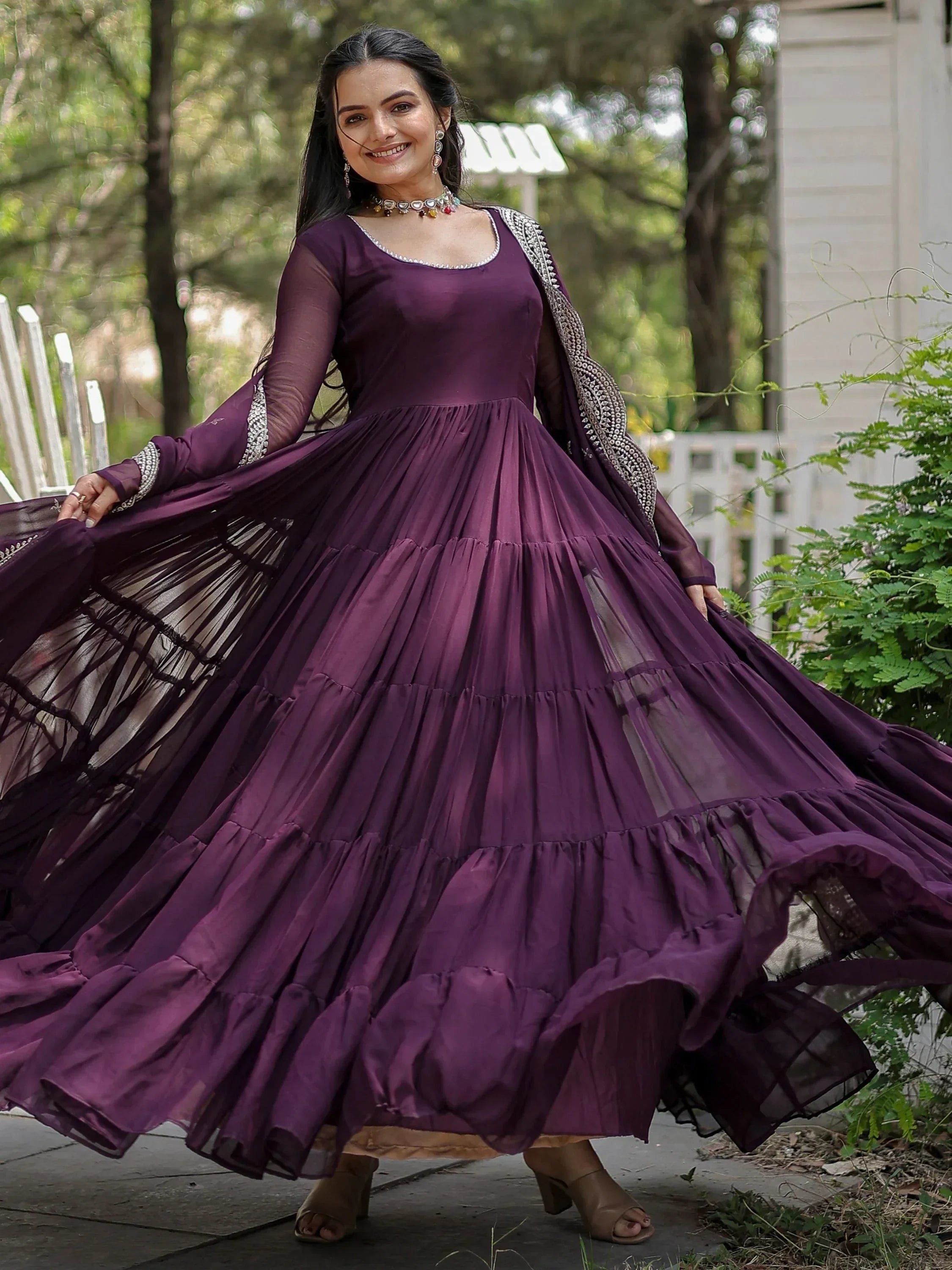 Woman in a purple ethnic gown twirling outdoors, wearing traditional jewelry