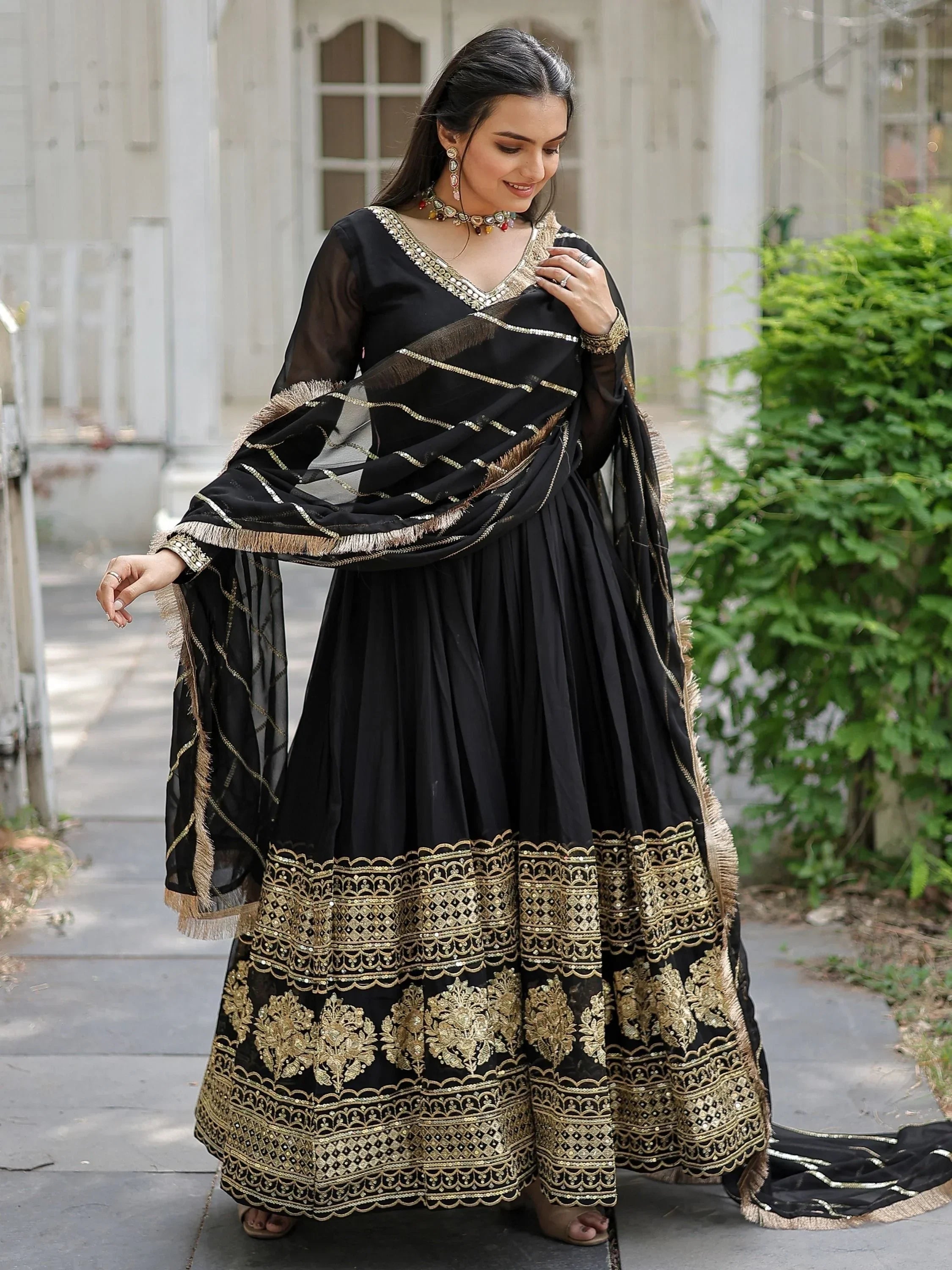 Woman wearing black and gold embroidered Anarkali gown with sheer dupatta outdoors