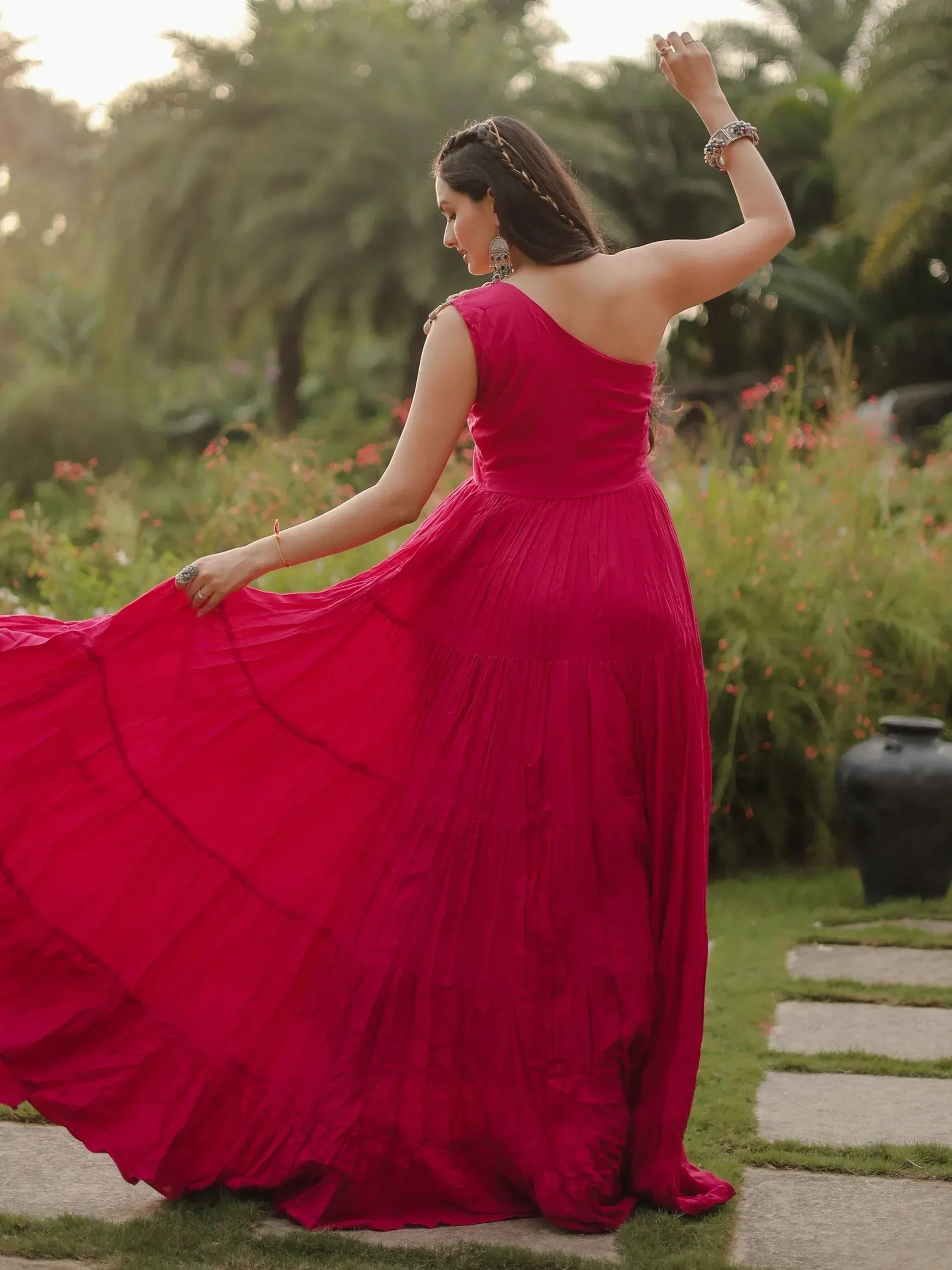 Woman in vibrant red ethnic gown twirling in garden, showcasing designer Indian wear
