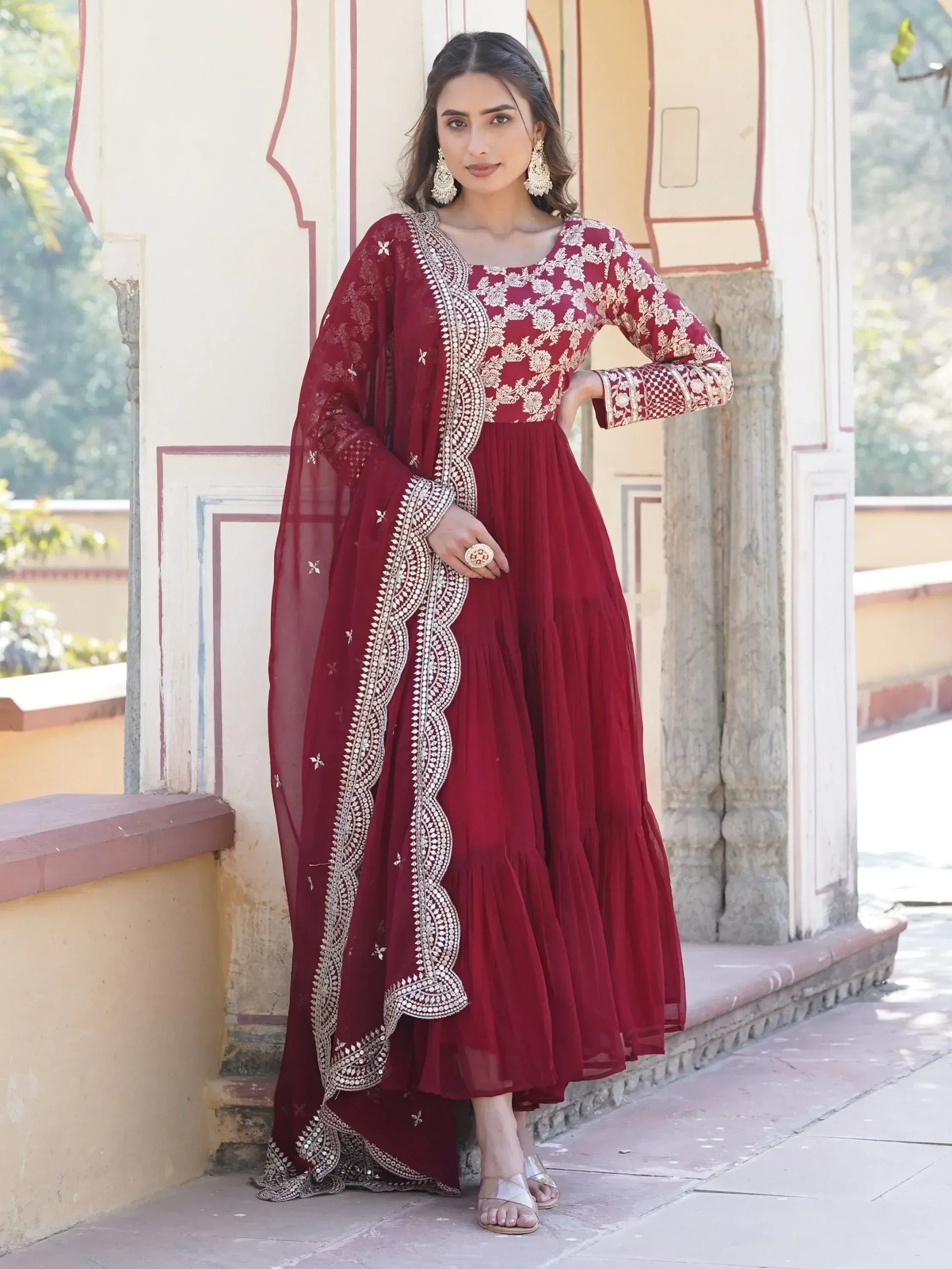 Woman wearing maroon embroidered Anarkali suit with dupatta, standing outdoors