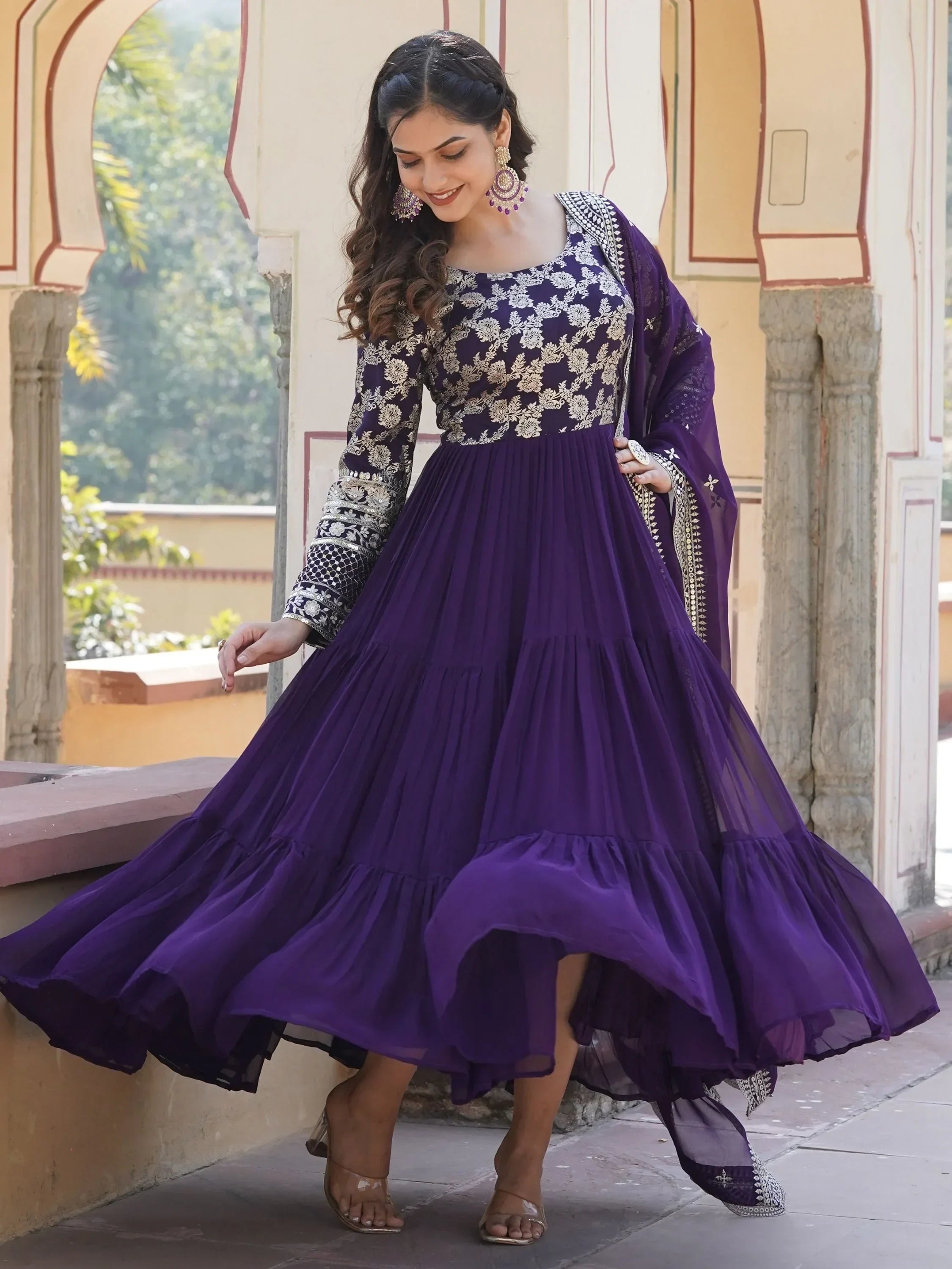 Woman wearing a purple embroidered ethnic gown with dupatta, standing outdoors