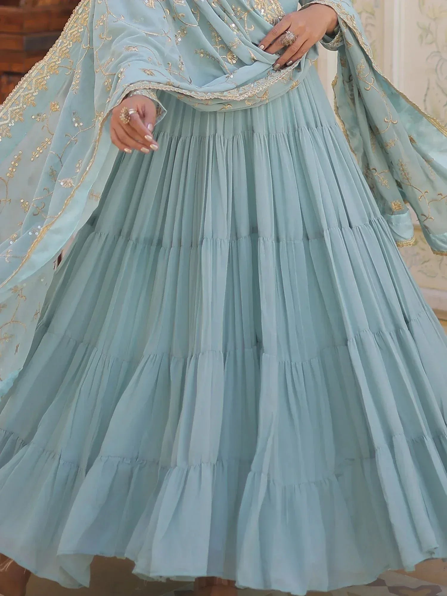 Light blue tiered ethnic gown with gold embroidery and sheer dupatta, perfect for Indian weddings or festive occasions.