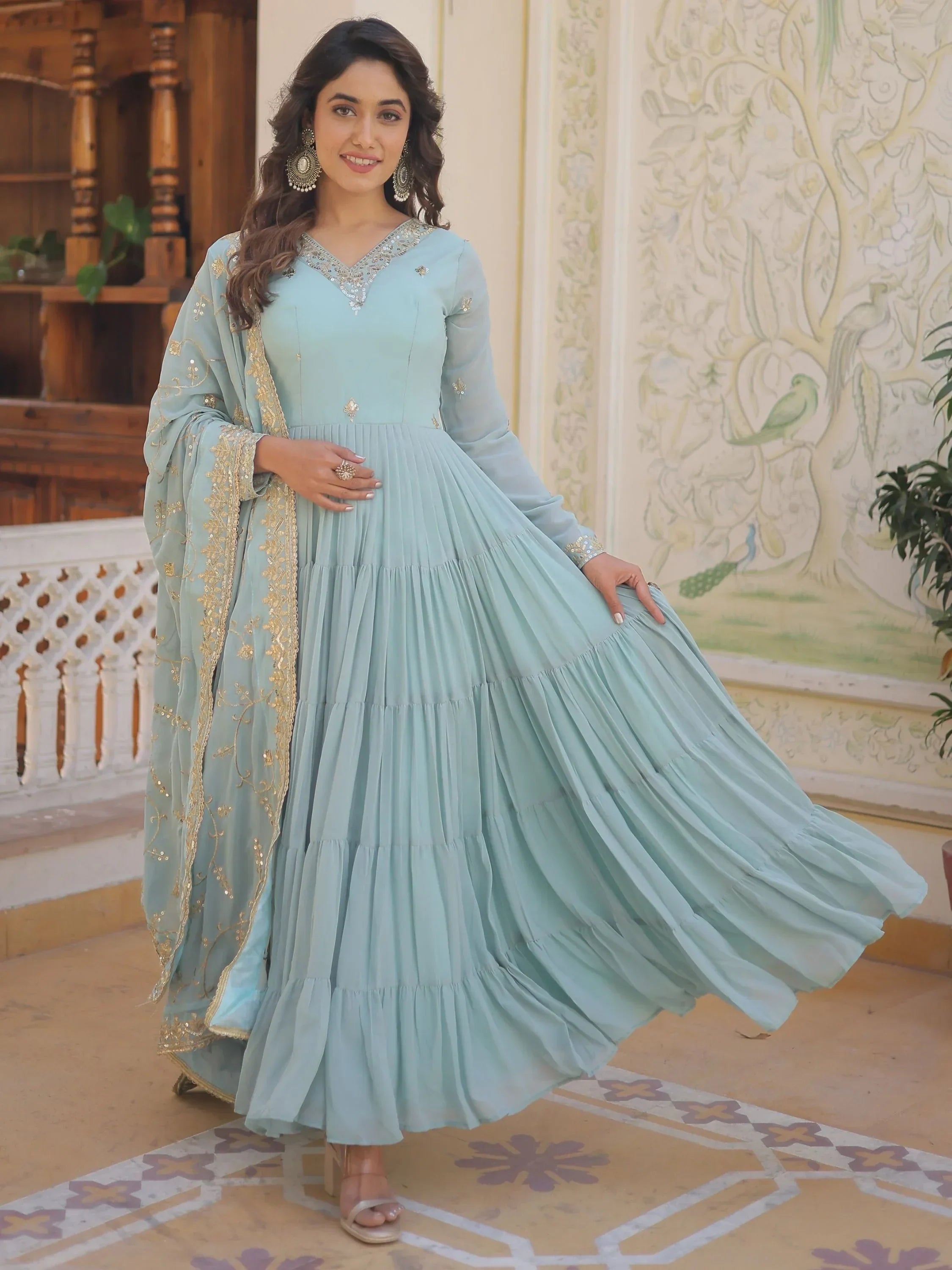 Woman in sky blue embroidered ethnic gown with dupatta, posing indoors elegantly