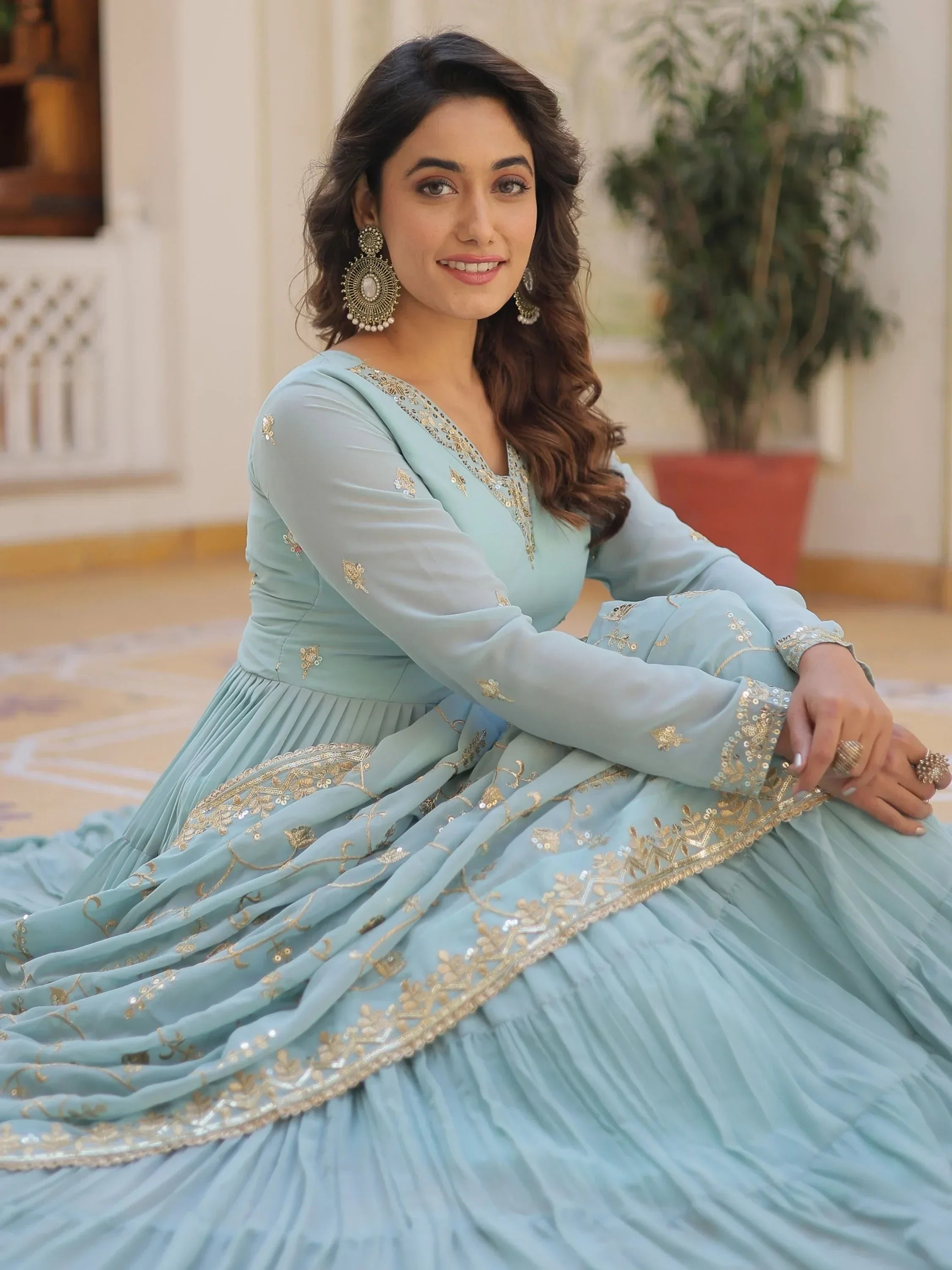 Woman in light blue lehenga gown with gold embroidery, traditional earrings, and indoor setting