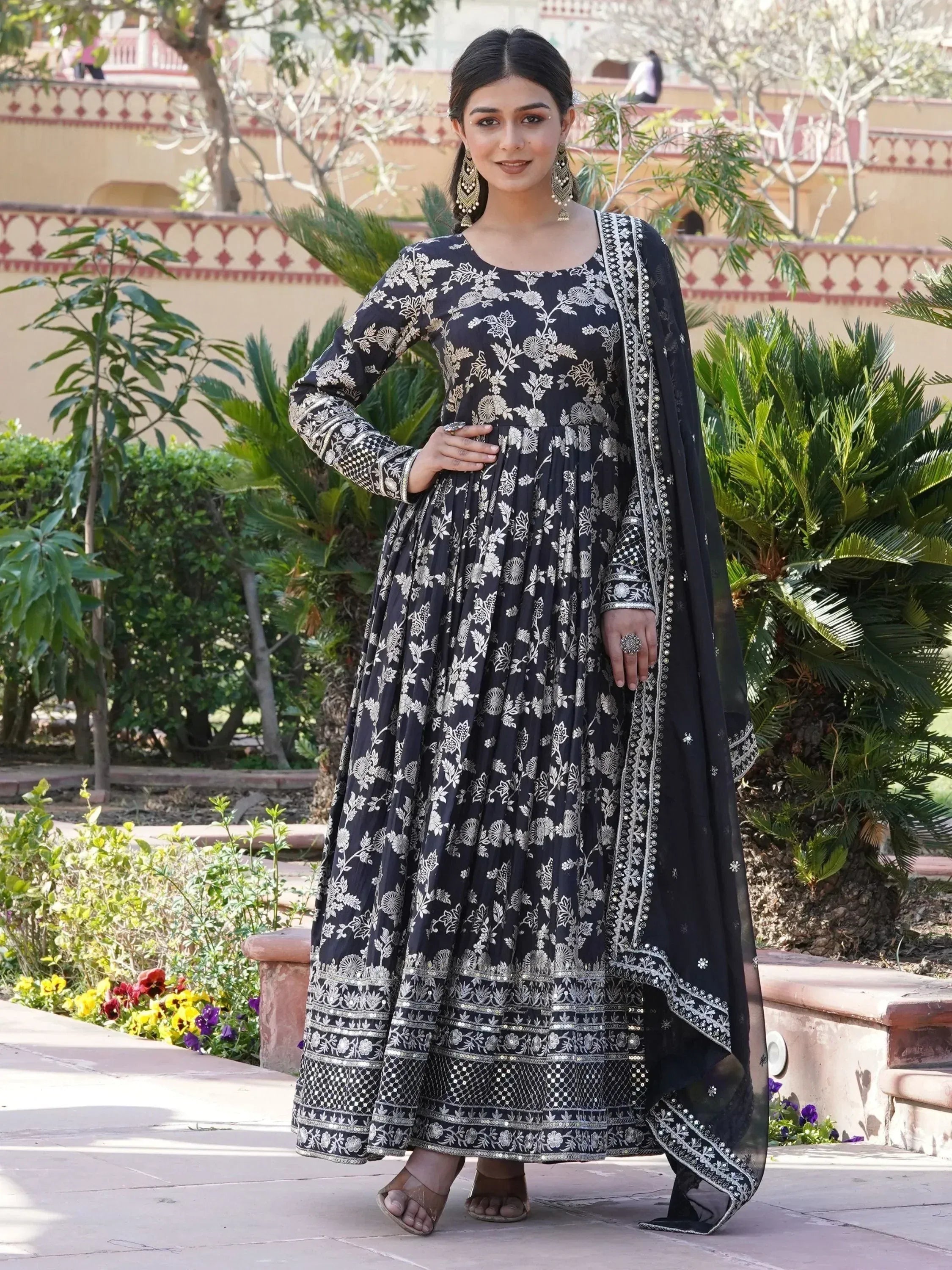 Woman wearing black floral embroidered Anarkali suit with dupatta in garden setting