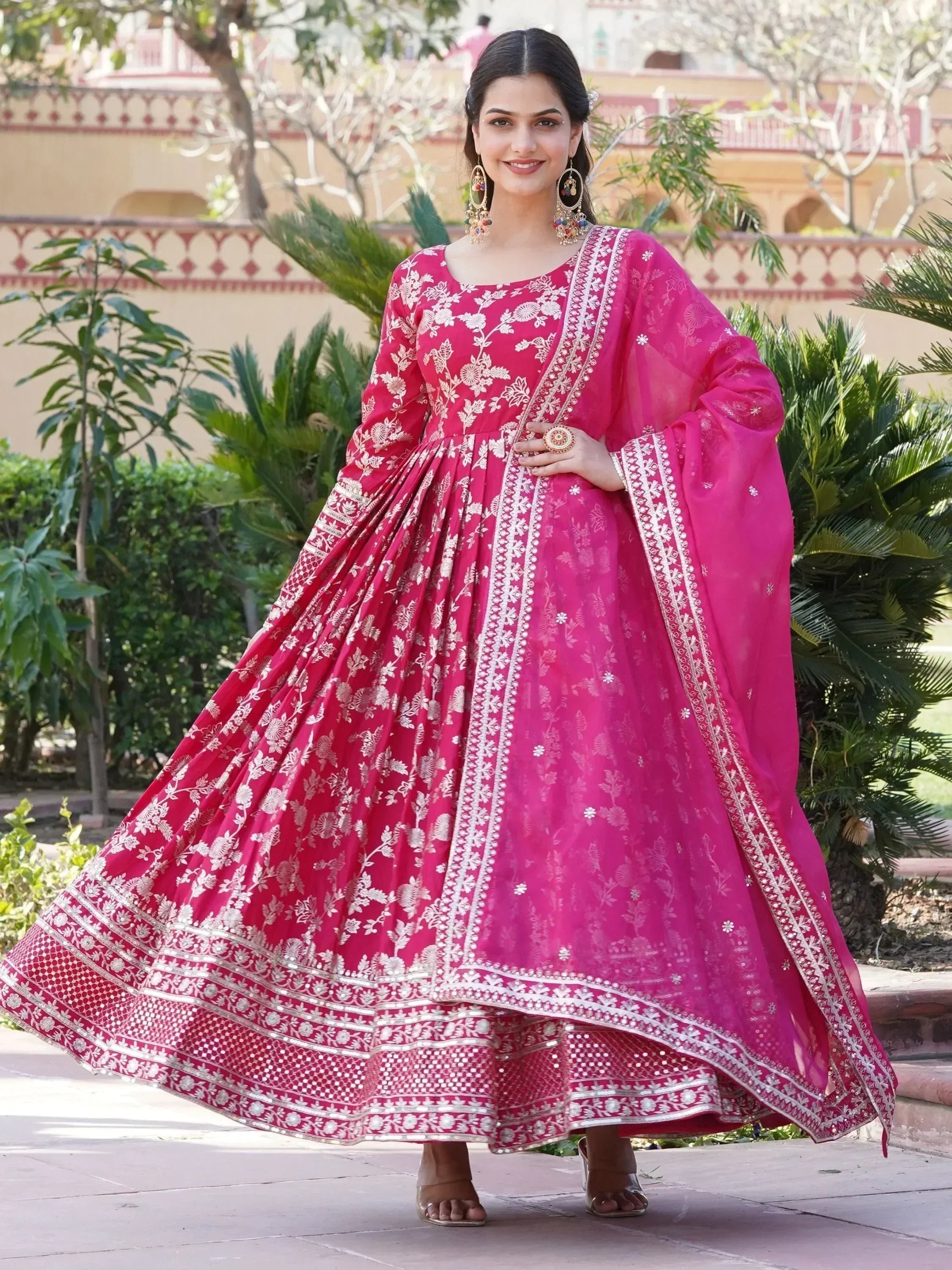 Woman wearing pink floral embroidered lehenga choli with dupatta, standing outdoors