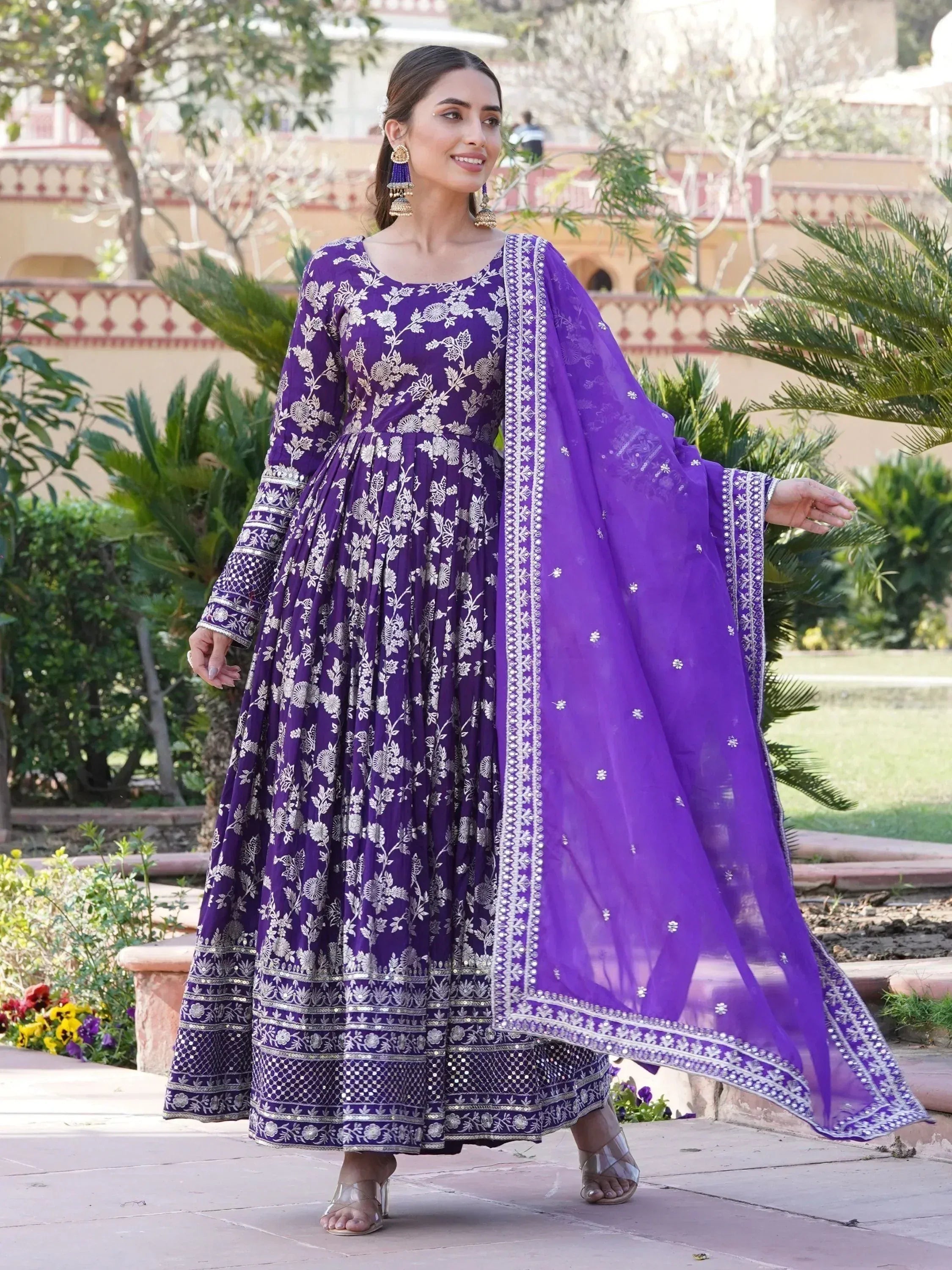 Woman wearing purple embroidered Anarkali gown with dupatta in garden setting