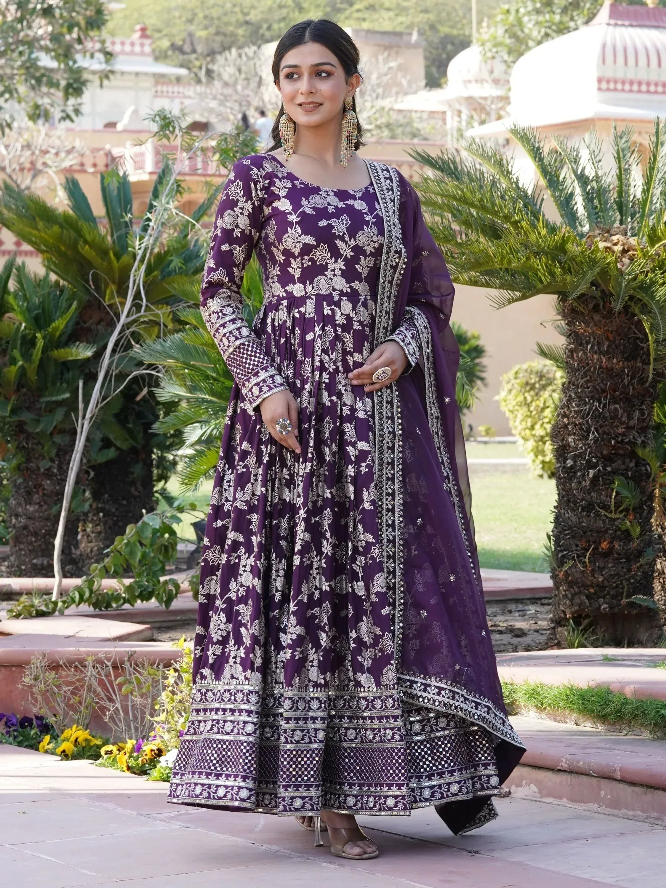 Woman wearing embroidered purple ethnic gown with dupatta, outdoor garden setting