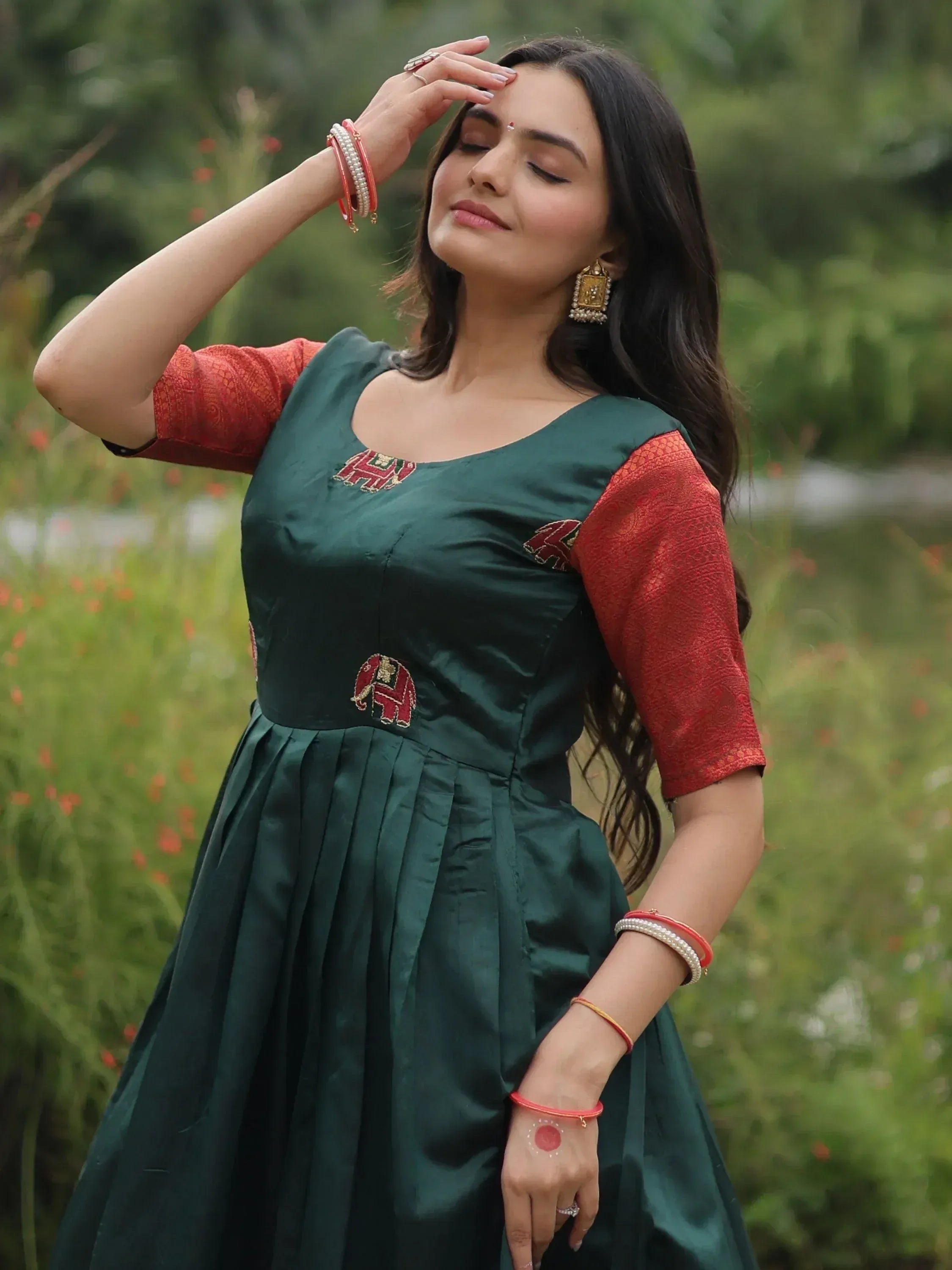 Woman in green ethnic gown with red sleeves and elephant embroidery, perfect for Indian festive occasions.