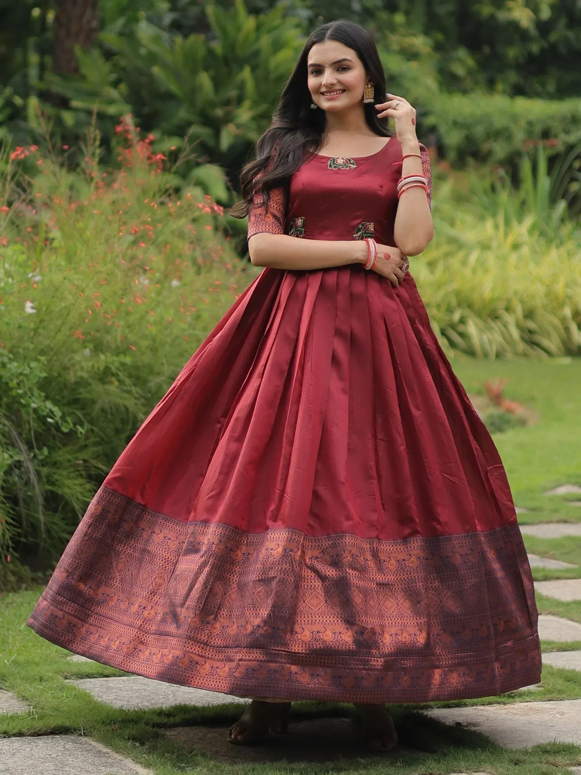 Woman in maroon ethnic gown with elephant embroidery and patterned border, perfect for Indian festive occasions