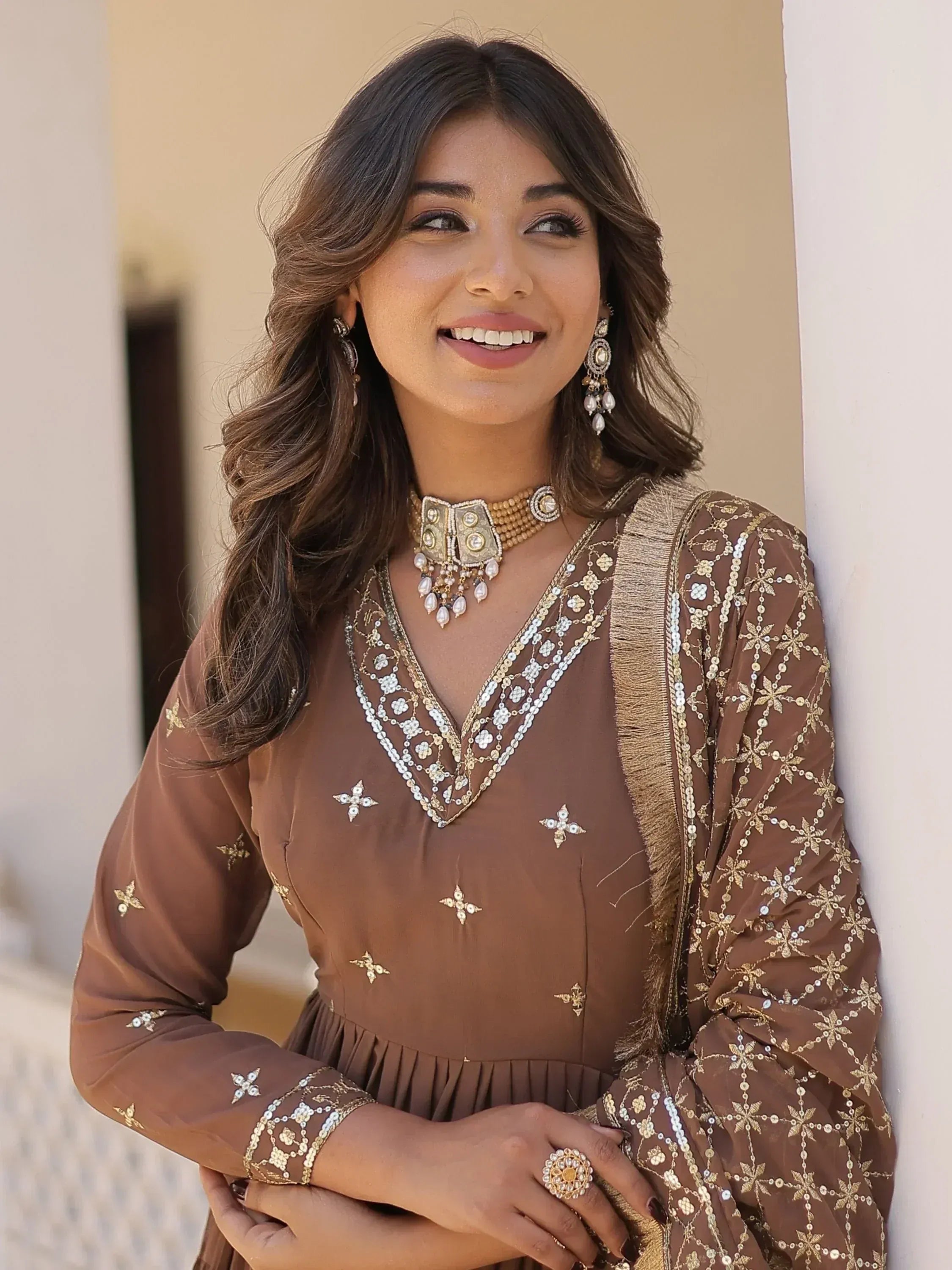 Brown embroidered ethnic gown with gold detailing, paired with traditional jewelry for festive occasions