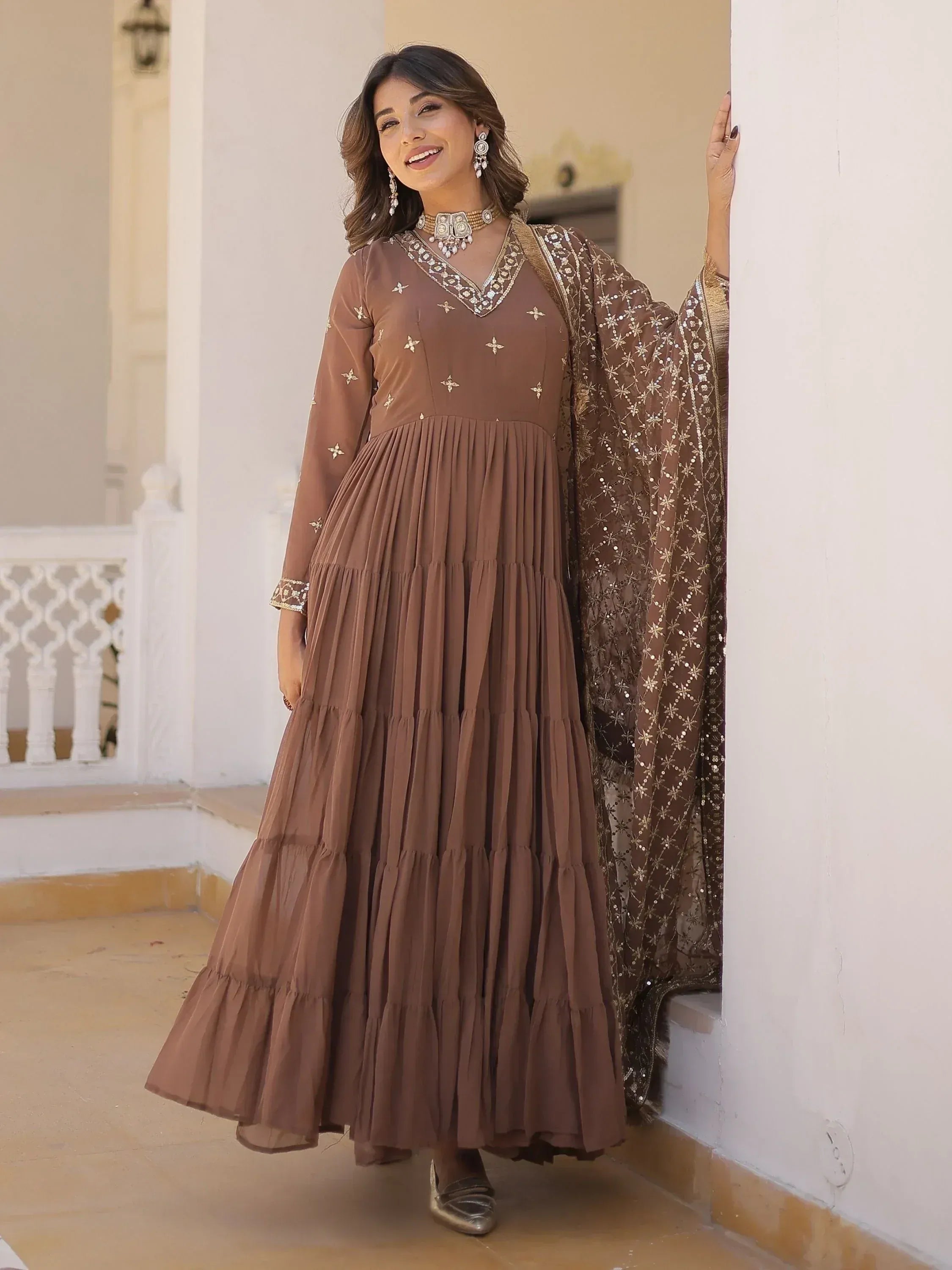 Brown ethnic gown with gold embroidery and pleated skirt, paired with matching dupatta for festive occasions