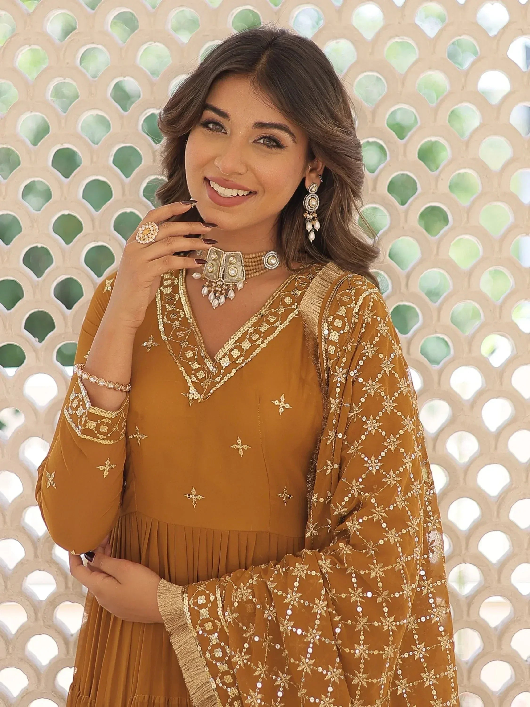 Woman in mustard ethnic gown with gold embroidery, traditional jewelry, and pleated skirt