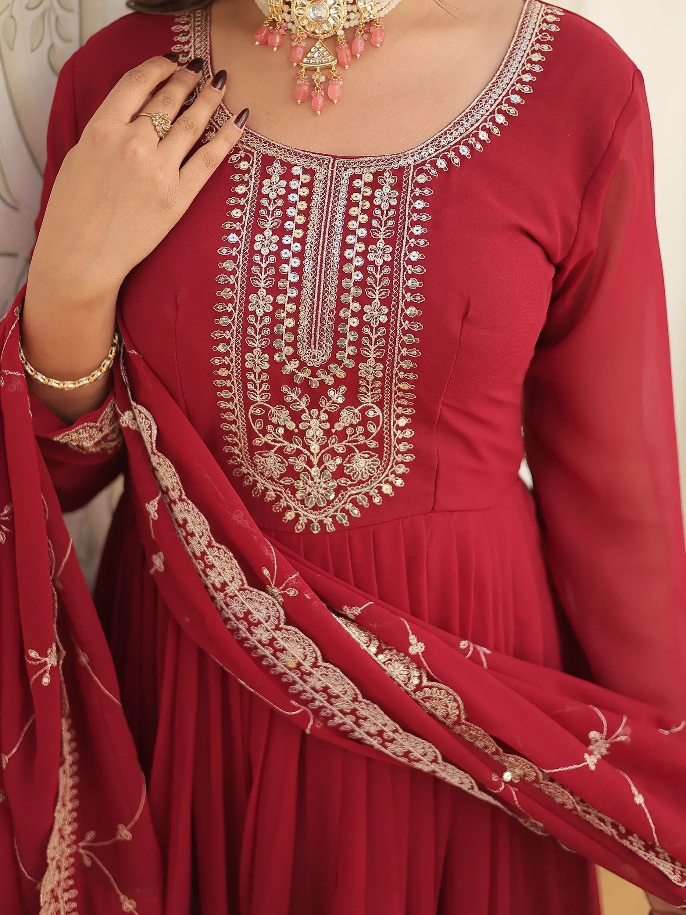 Red ethnic gown with gold embroidery, matching dupatta, and traditional jewelry for Indian wear