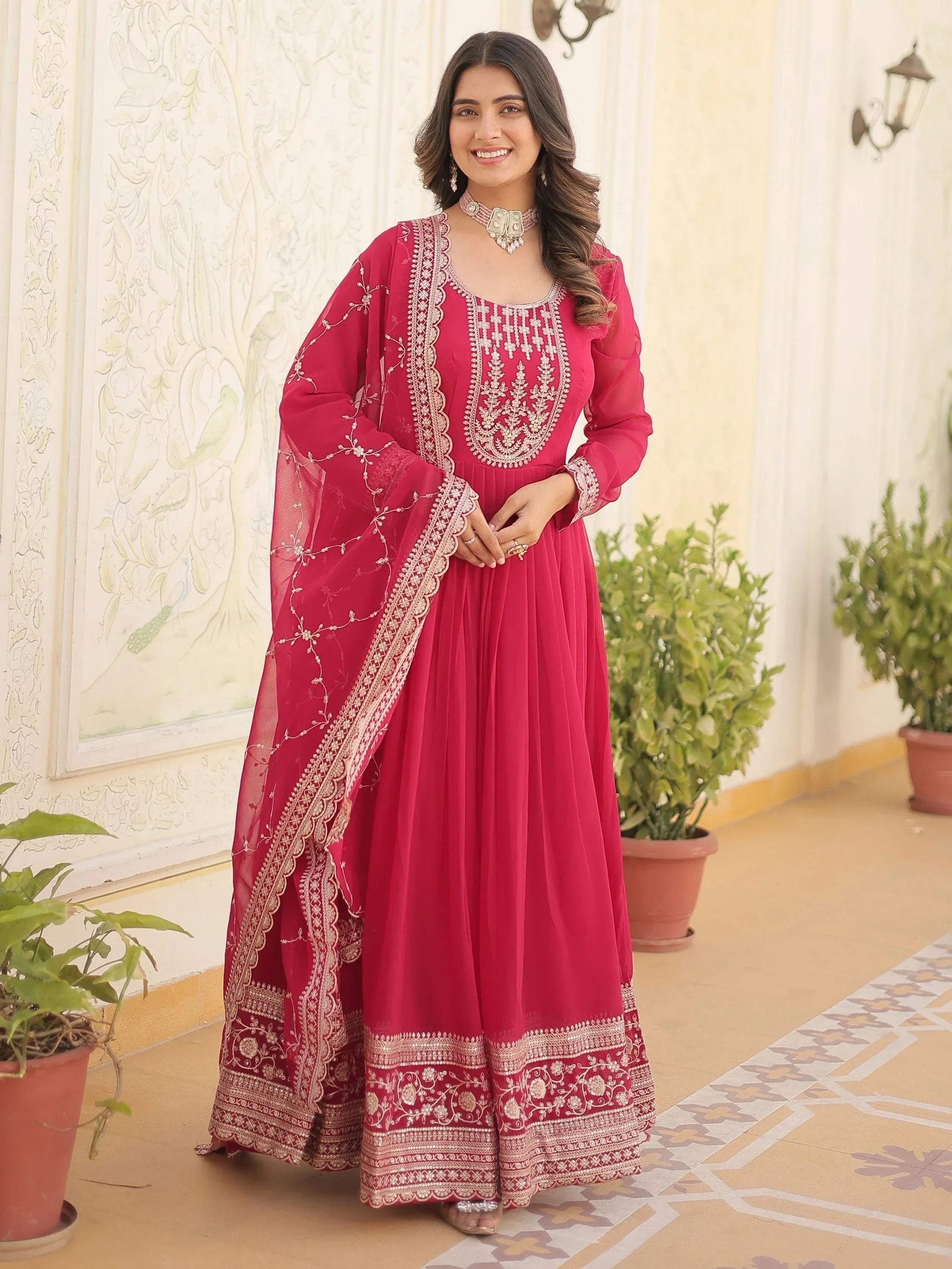 Woman in a pink embroidered ethnic gown with dupatta, standing outdoors, smiling