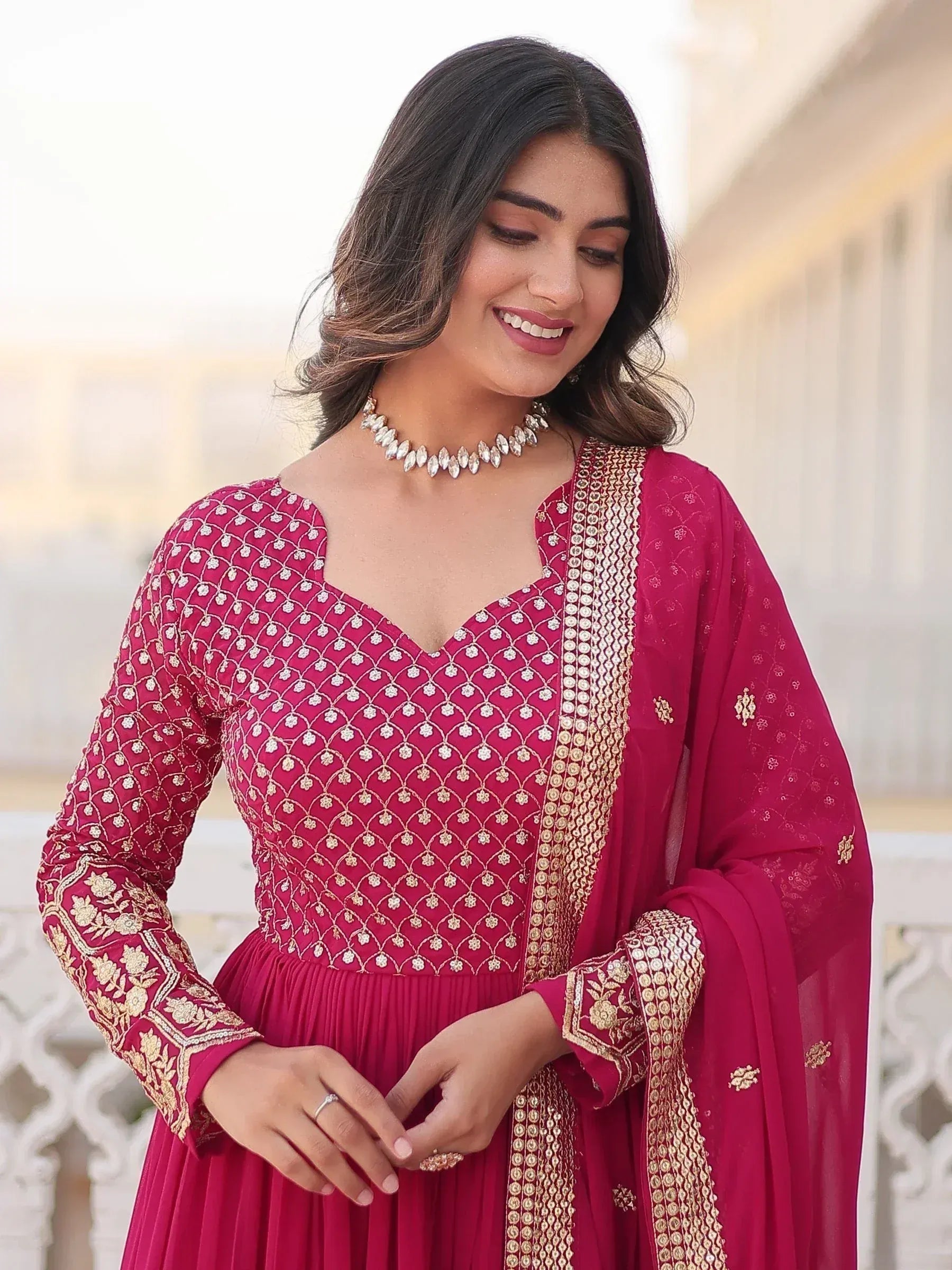 Woman in elegant maroon ethnic gown with gold embroidery and matching dupatta, perfect for Indian celebrations.