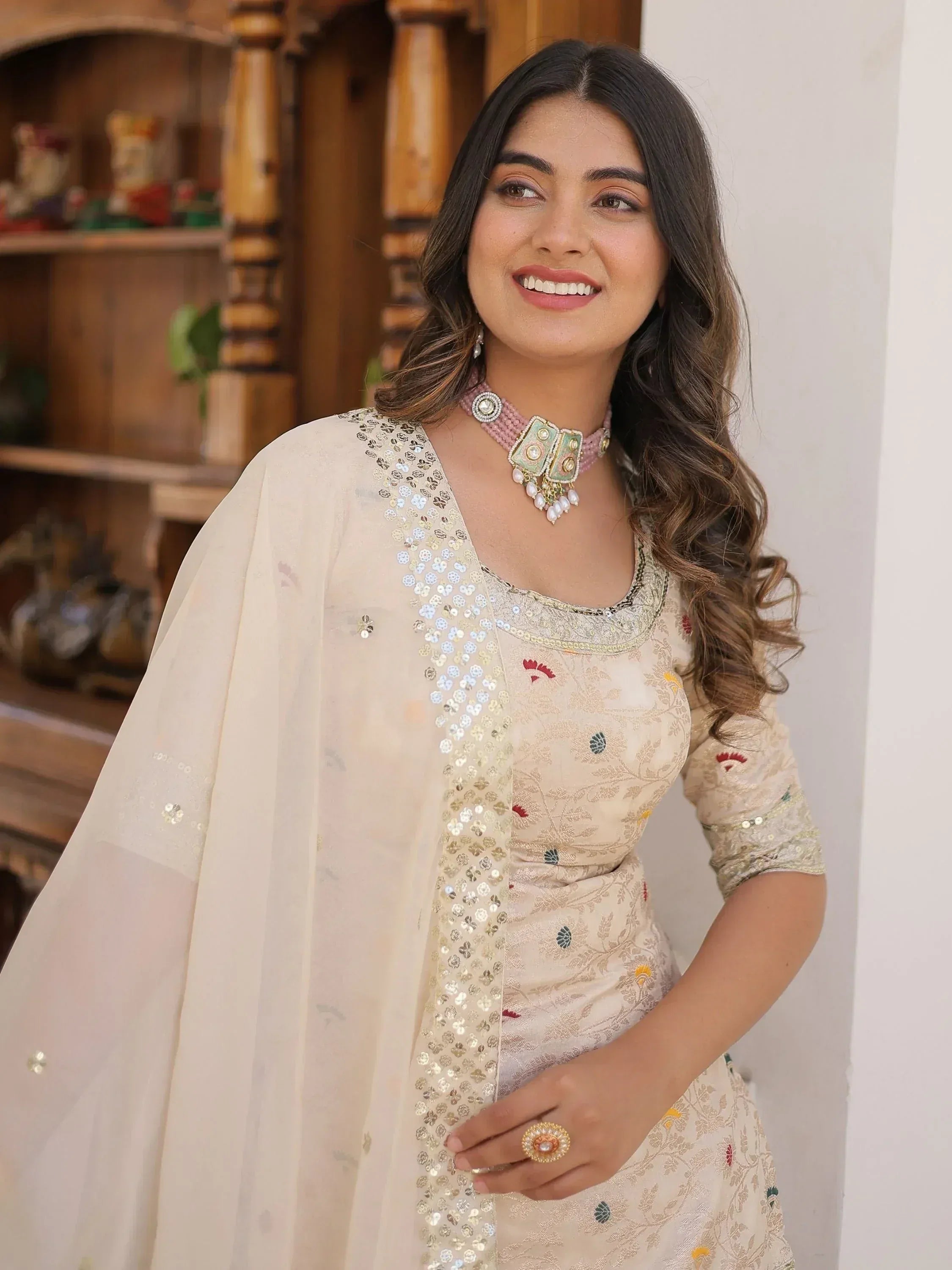 Woman in elegant cream ethnic gown with floral embroidery and sequin dupatta, styled with traditional jewelry
