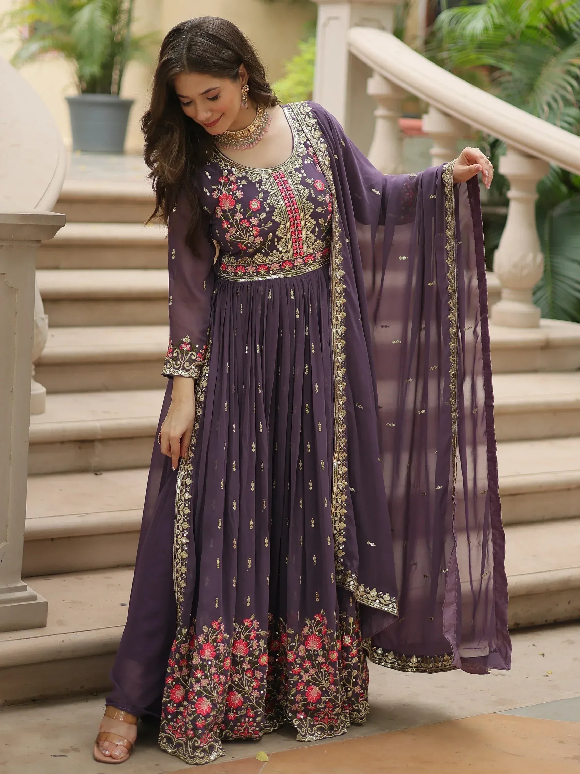 Woman wearing purple embroidered Anarkali suit with floral dupatta, standing on stairs