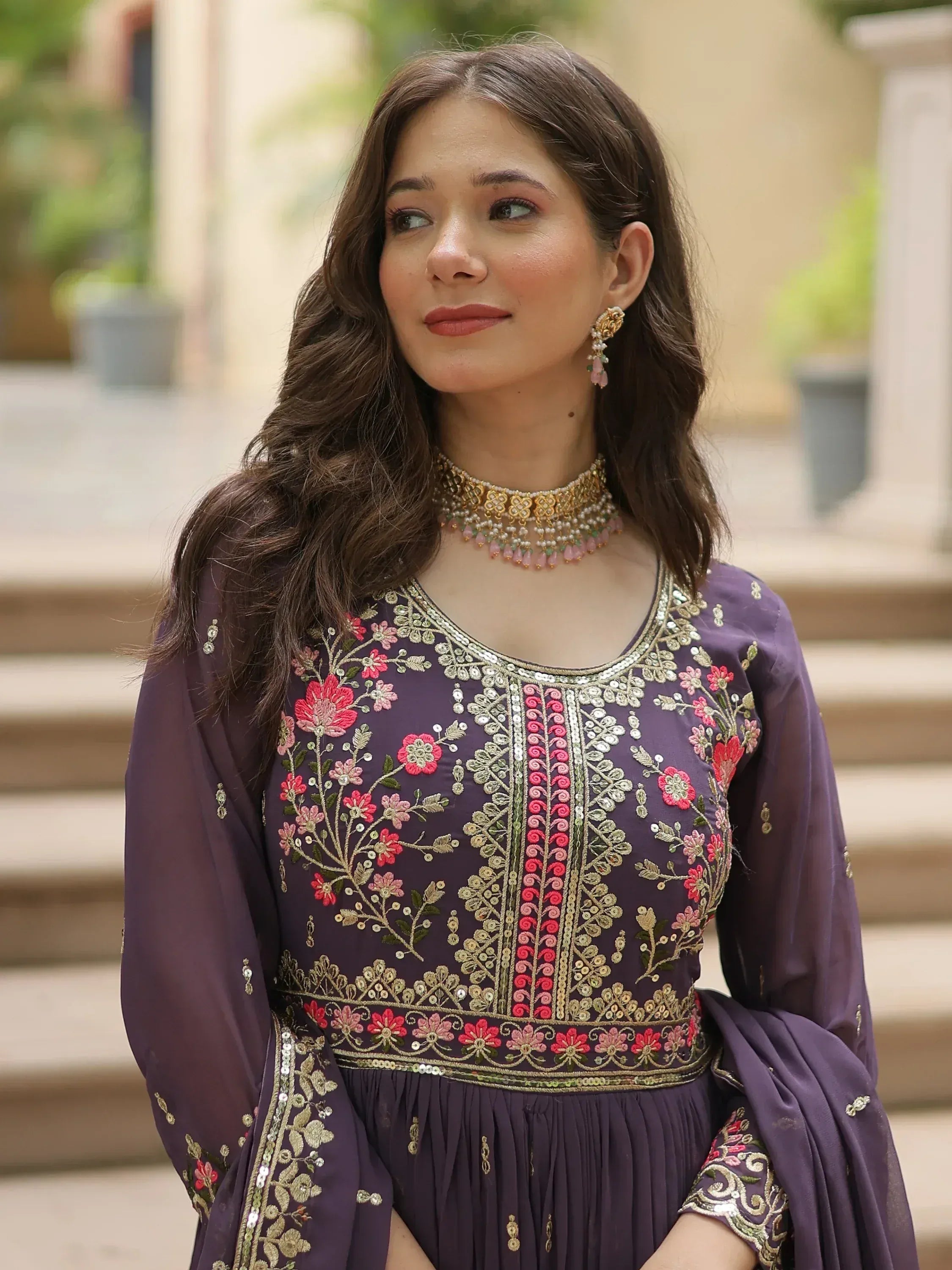 Woman in a purple embroidered ethnic gown with floral designs, wearing traditional jewelry