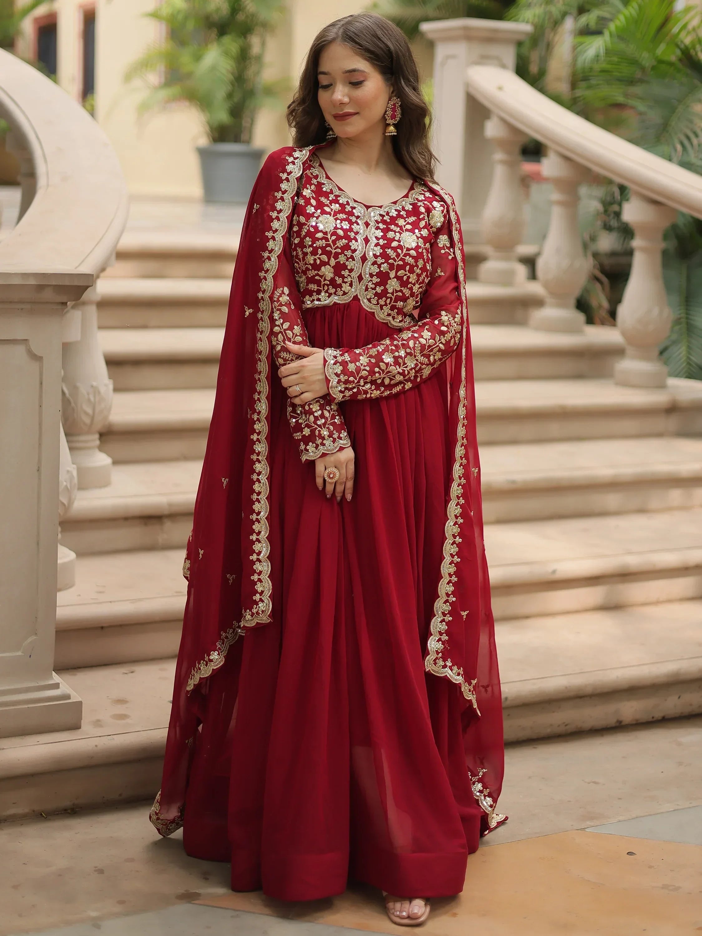 Woman in red embroidered ethnic gown with dupatta standing on outdoor steps