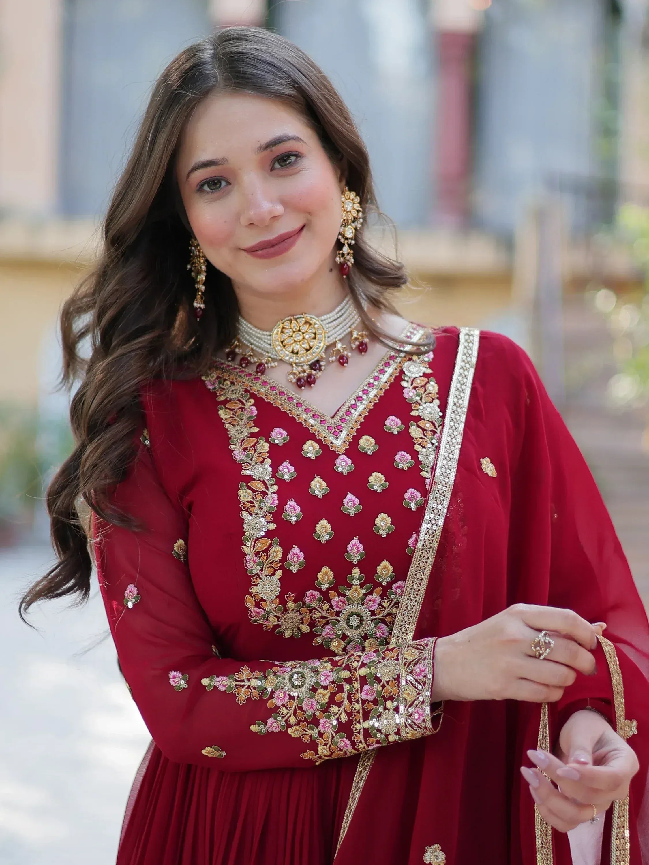 Woman in maroon embroidered ethnic gown with floral detailing and gold jewelry, perfect for Indian occasions.