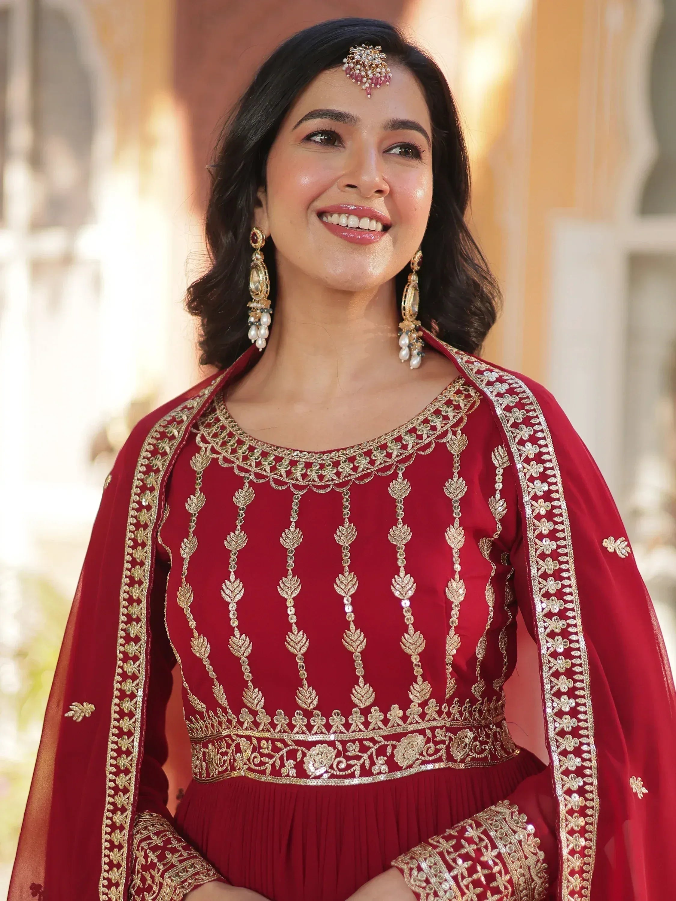 Woman in maroon ethnic gown with gold embroidery, perfect for Indian weddings or festive occasions.