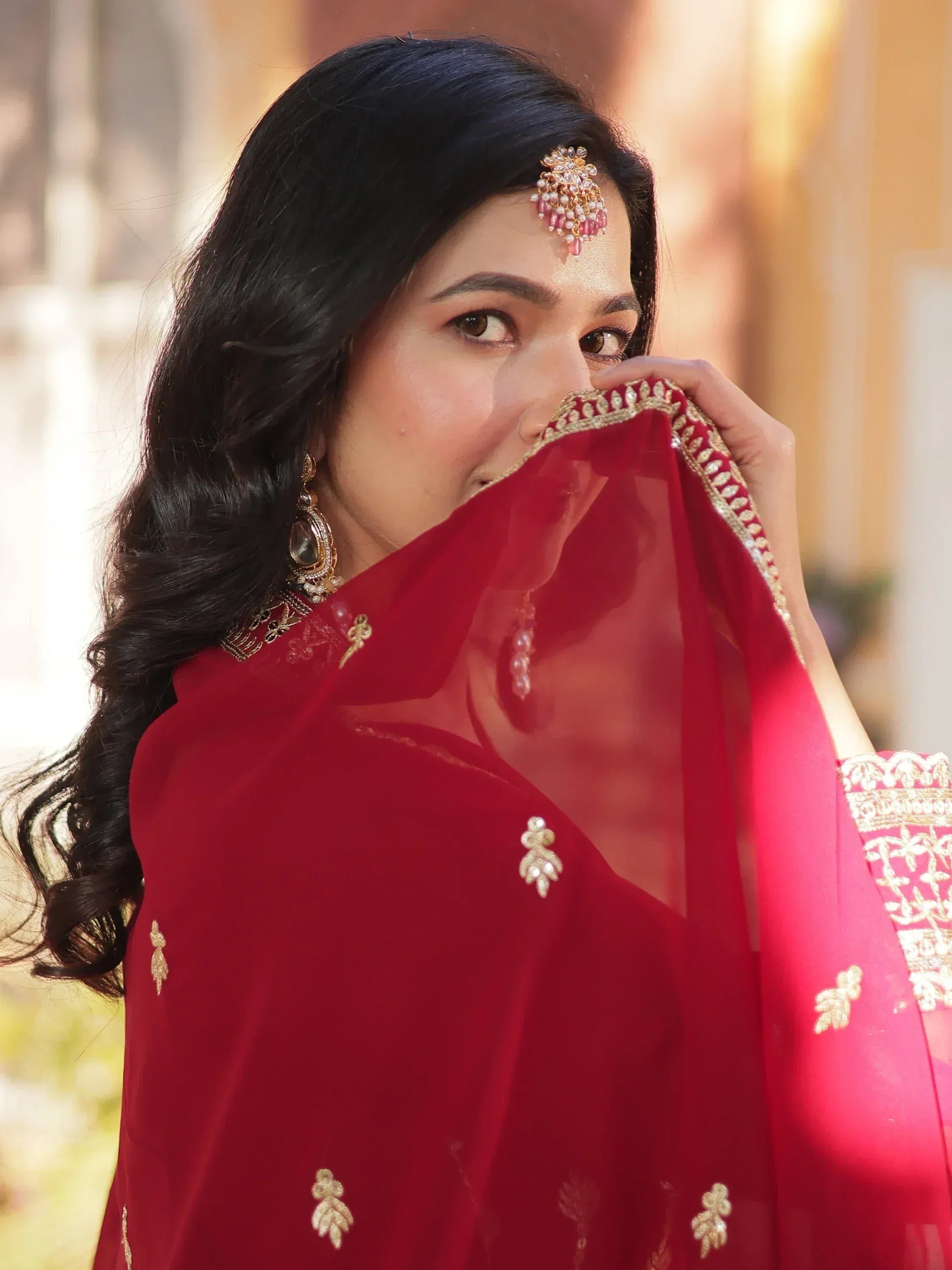 Woman in red ethnic saree with gold embroidery and traditional jewelry, perfect for Indian weddings or festive occasions.
