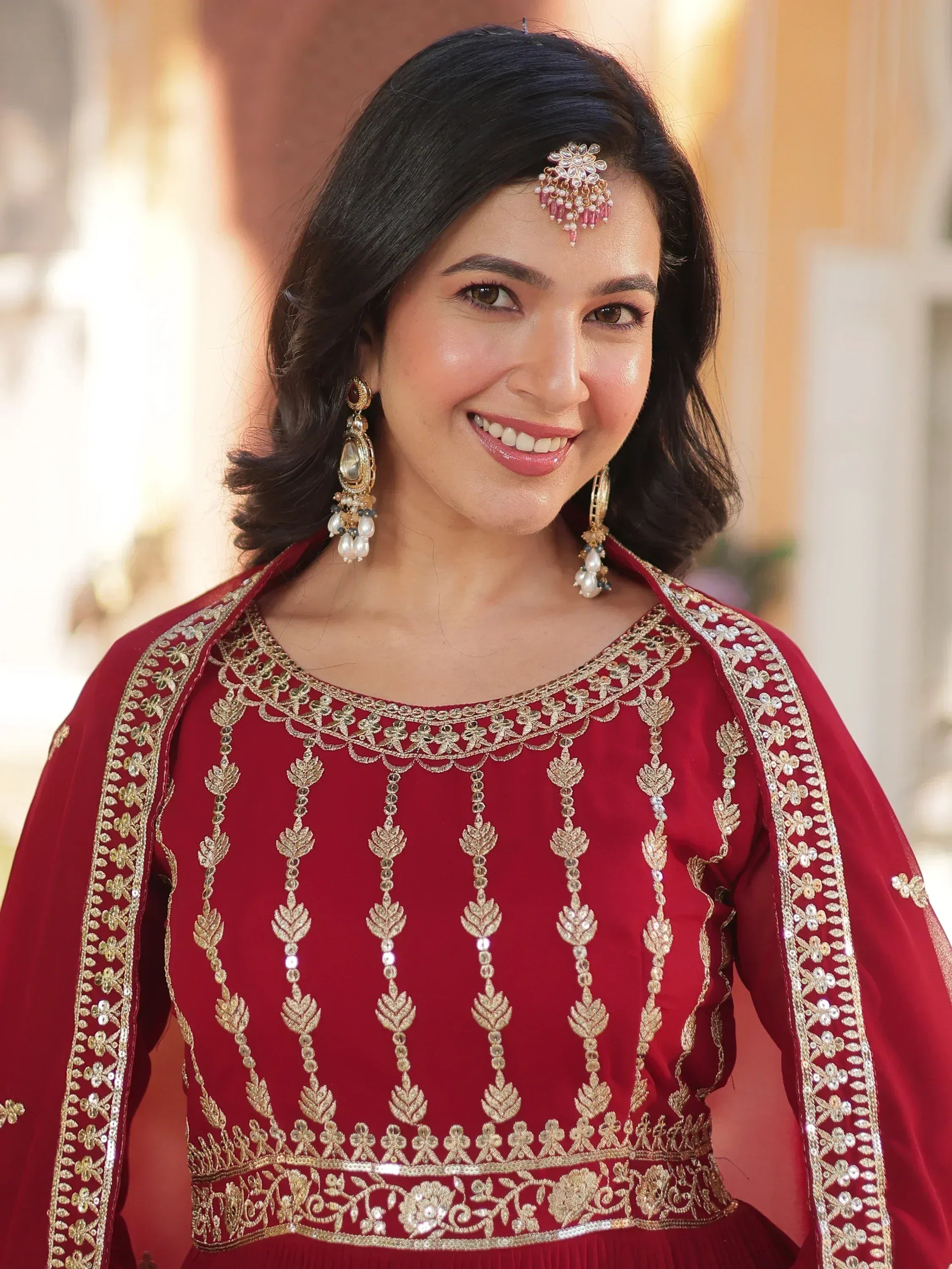 Woman in maroon ethnic gown with gold embroidery and traditional jewelry for Indian occasions