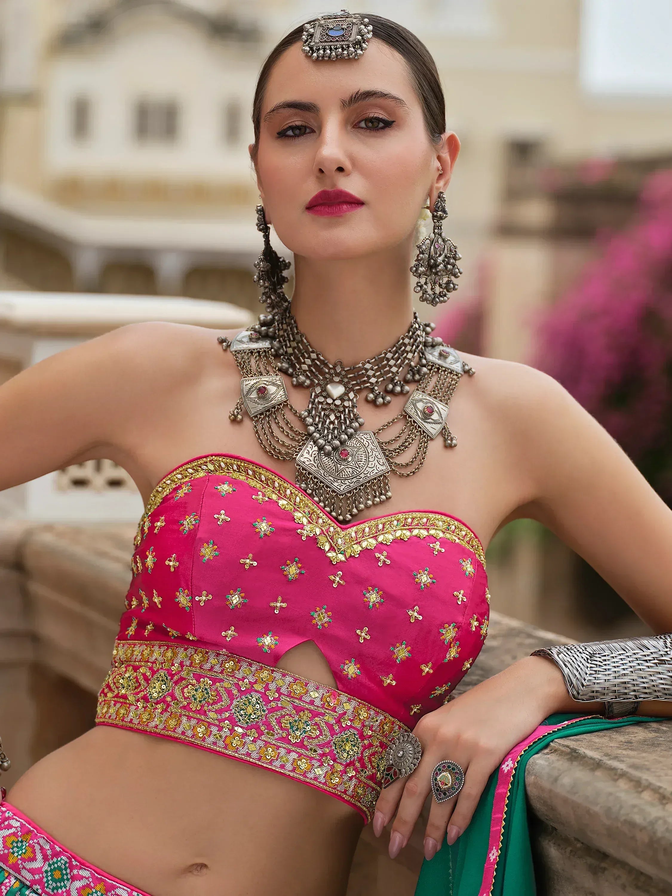 Pink embroidered lehenga choli with gold detailing, paired with traditional Indian jewelry and green dupatta.