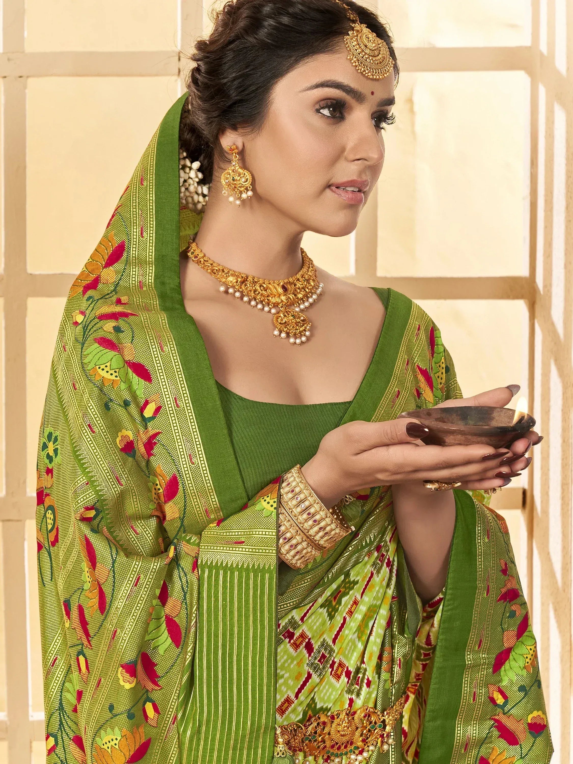 Woman in green floral saree with gold jewelry holding diya, traditional Indian ethnic wear